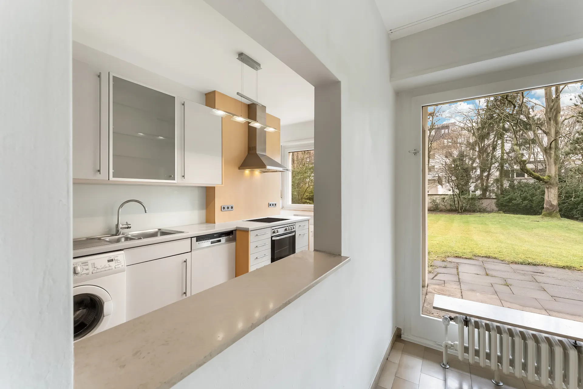 Moderne Küche mit Geräten und Blick auf einen Garten durch ein großes Fenster.