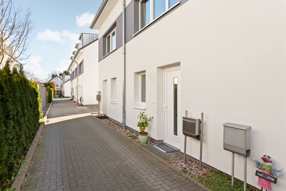 Gepflasterter Weg entlang moderner Wohnhäuser mit Briefkästen und einer kleinen Pflanze vor der Tür.