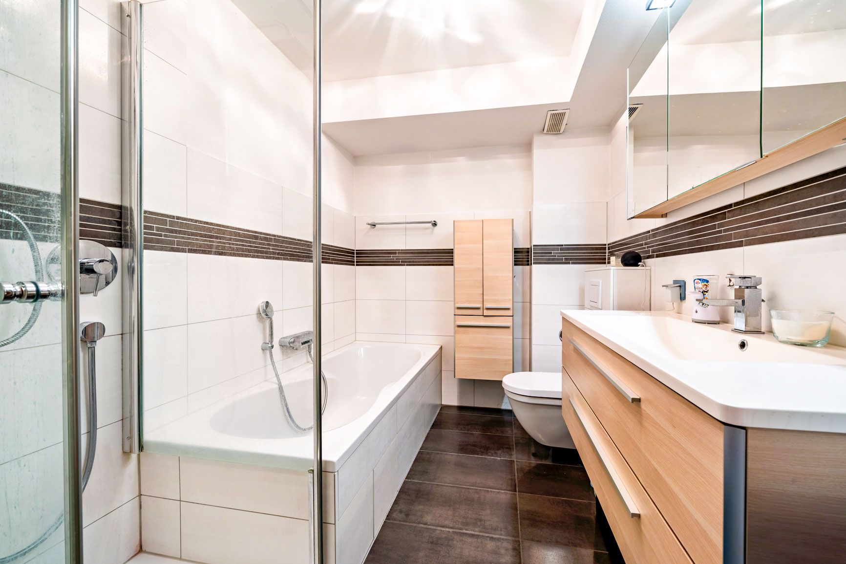 Modernes Badezimmer mit Badewanne, Dusche, Waschbecken und Holzschränken.
