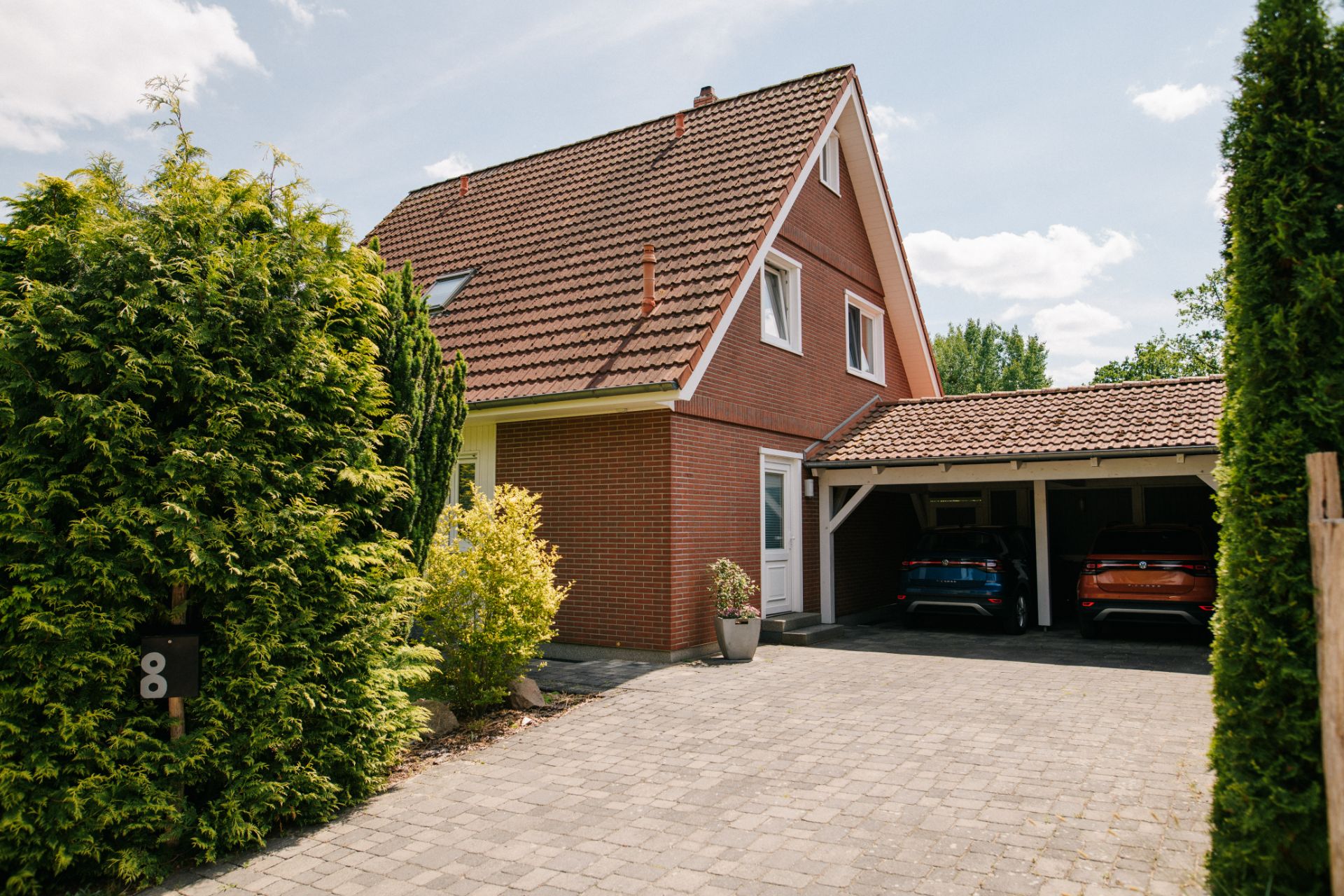 Einfamilienhaus mit rotem Dach, Auffahrt und Doppelgarage mit zwei Autos.