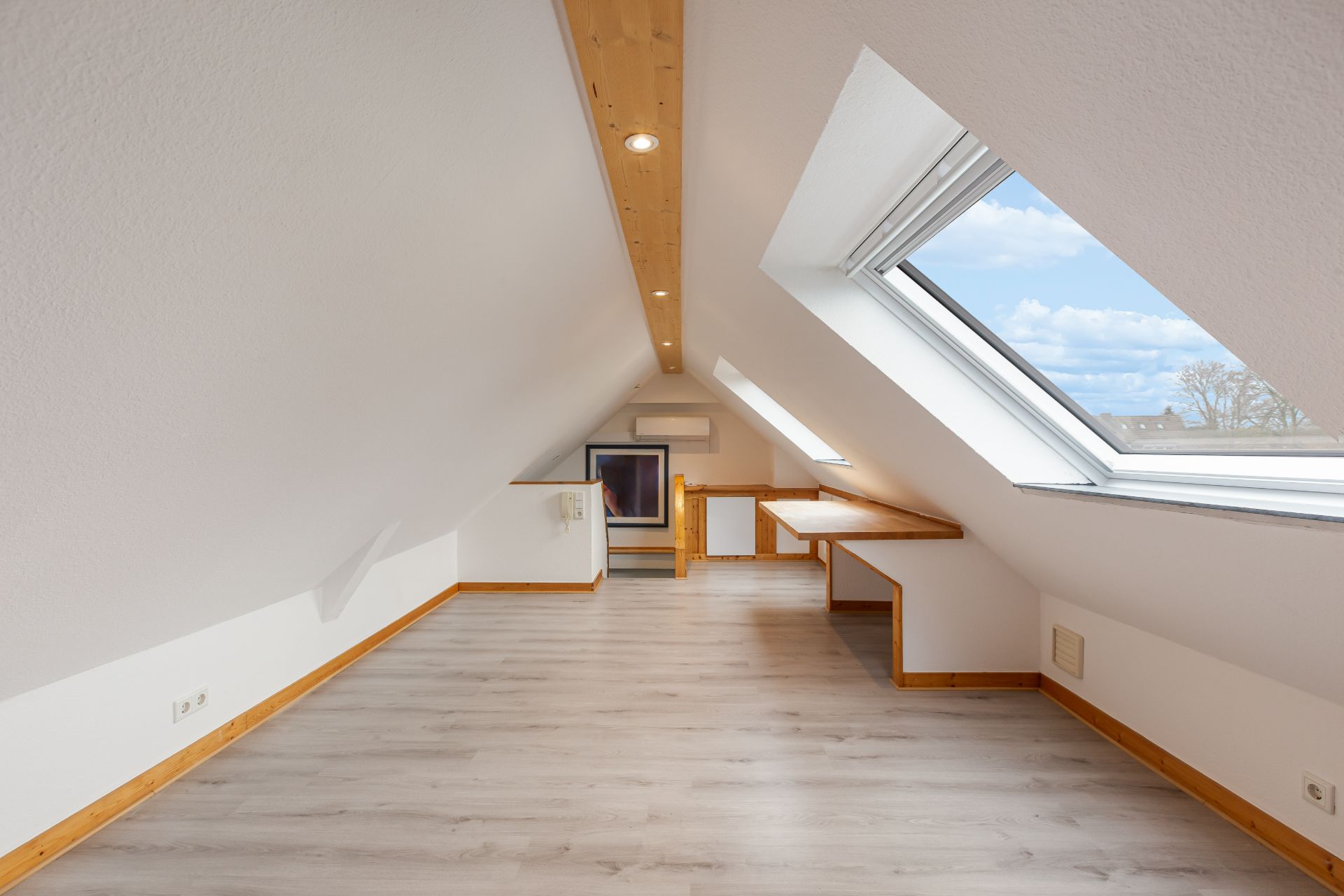 Heller Dachbodenraum mit schrägen Wänden, großem Dachfenster und Holzdetails.