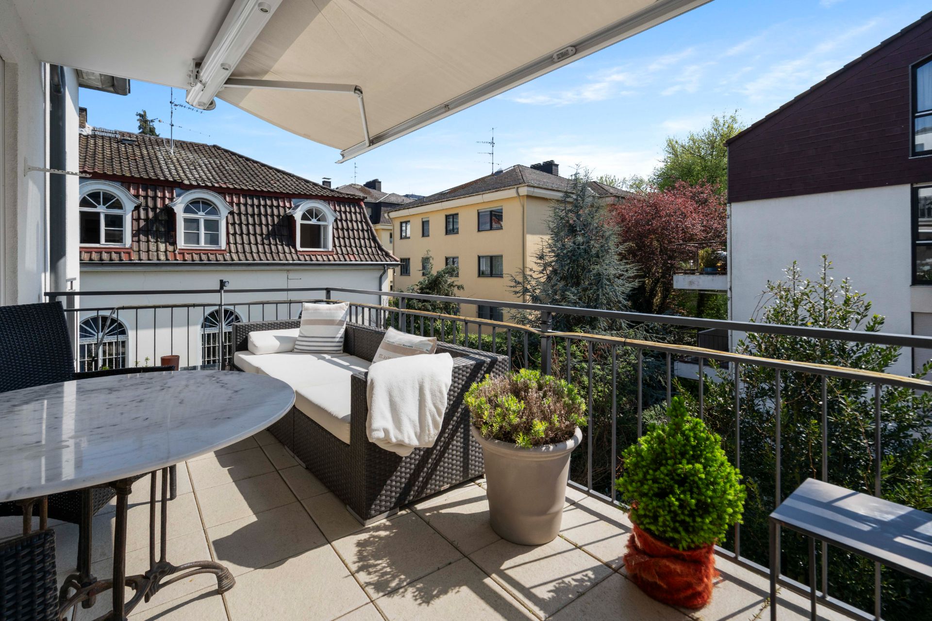 Balkon mit Sofa, Tisch, Pflanzen und Blick auf Nachbarhäuser.