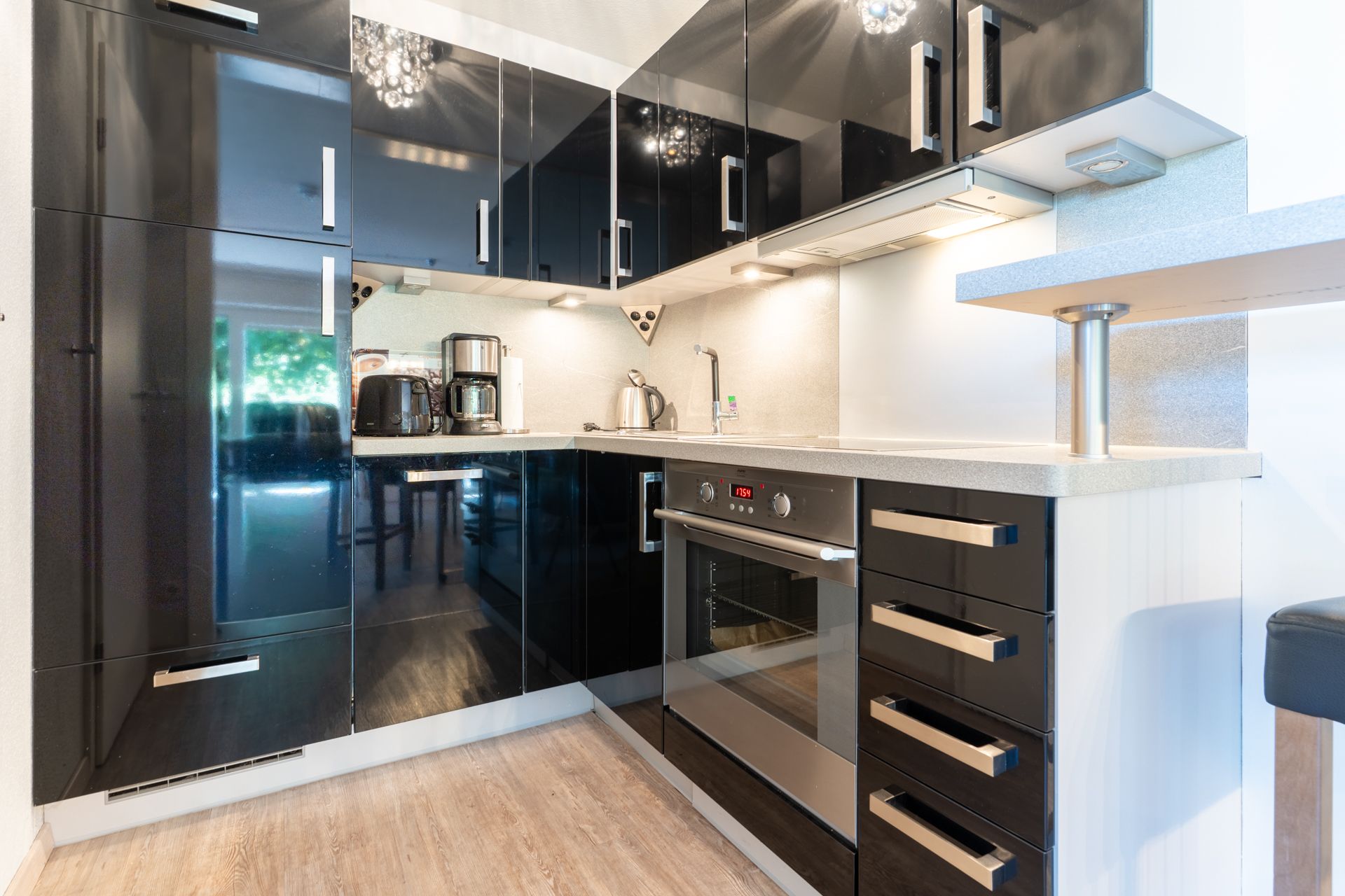 Moderne Einbauküche mit schwarzen Hochglanzschränken, Backofen und Kaffeemaschine.