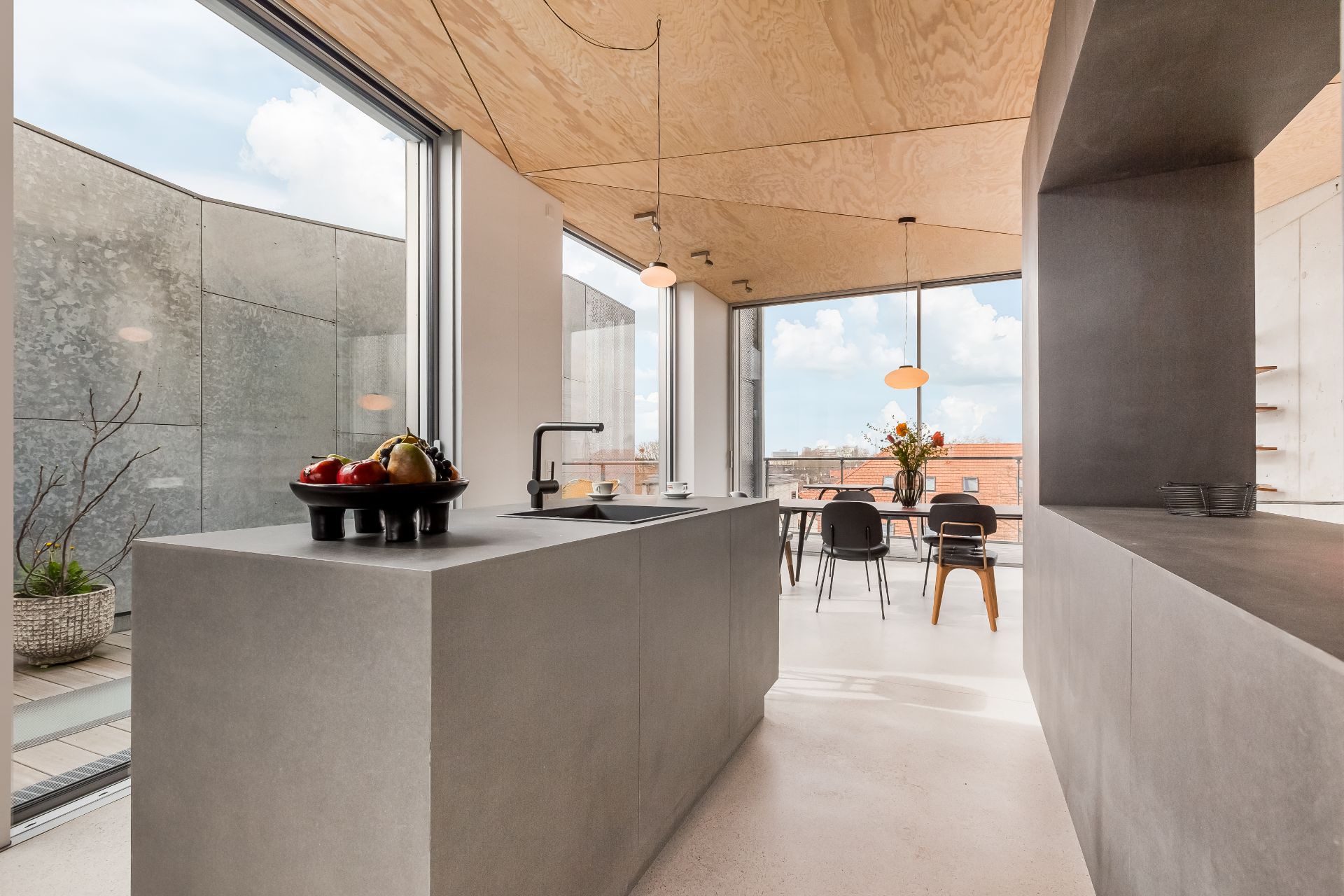 Moderne Küche mit grauer Kochinsel und großem Fenster, dahinter ein Esstisch mit schwarzen Stühlen.
