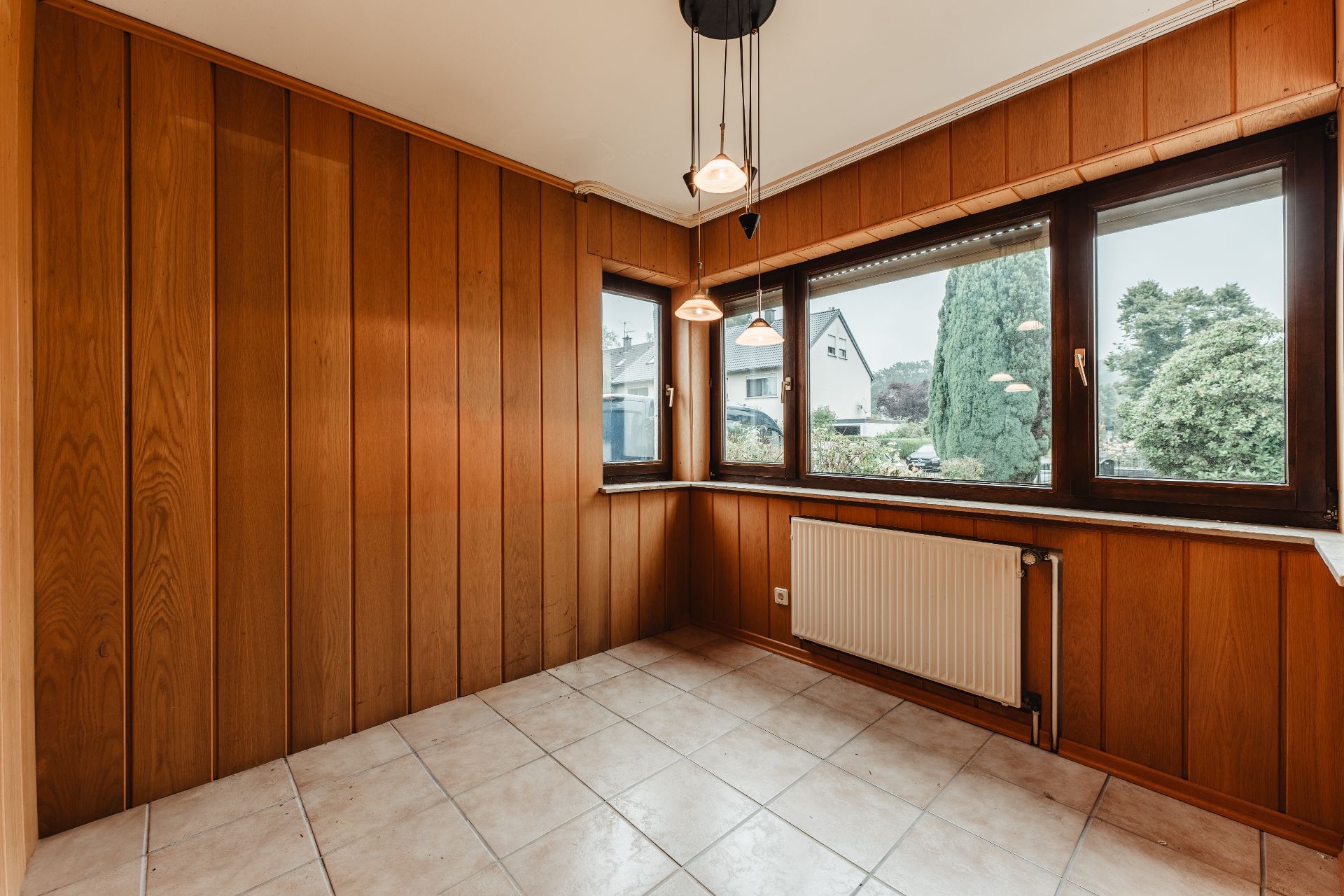 Leerer Raum mit Holzverkleidung, Fliesenboden, großen Fenstern und Heizkörper.