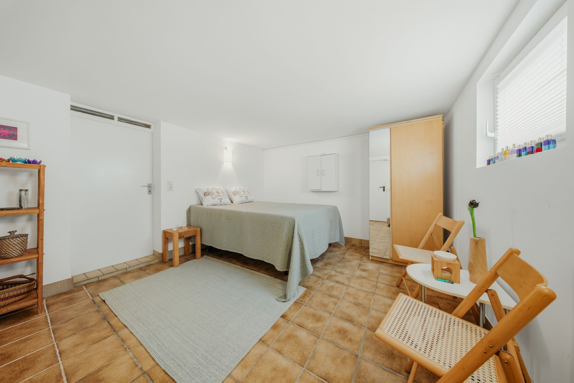 Helles Schlafzimmer mit Doppelbett, Holzmöbeln, Teppich und zwei Fenstern.