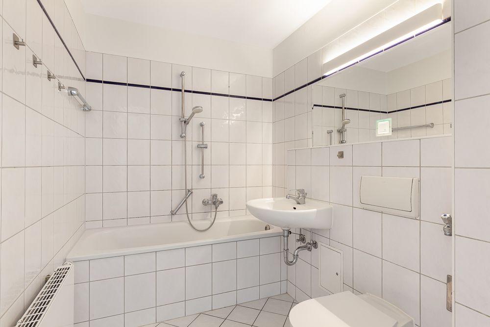 Helles Badezimmer mit Badewanne, Waschbecken, Toilette und Spiegel, alles weiß gefliest.