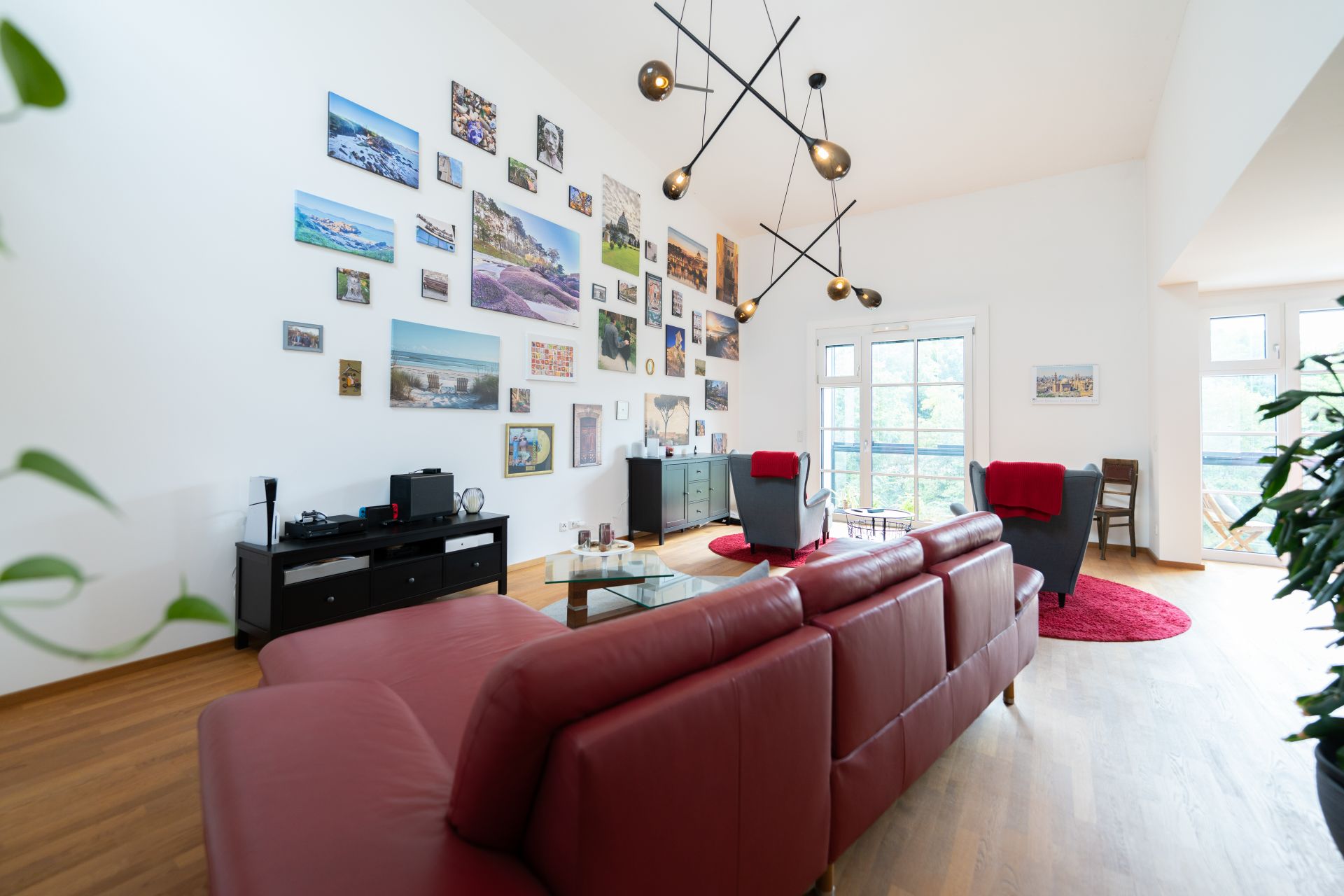 Modernes Wohnzimmer mit rotem Sofa, Sessel, Wandbildern und großen Fenstern.