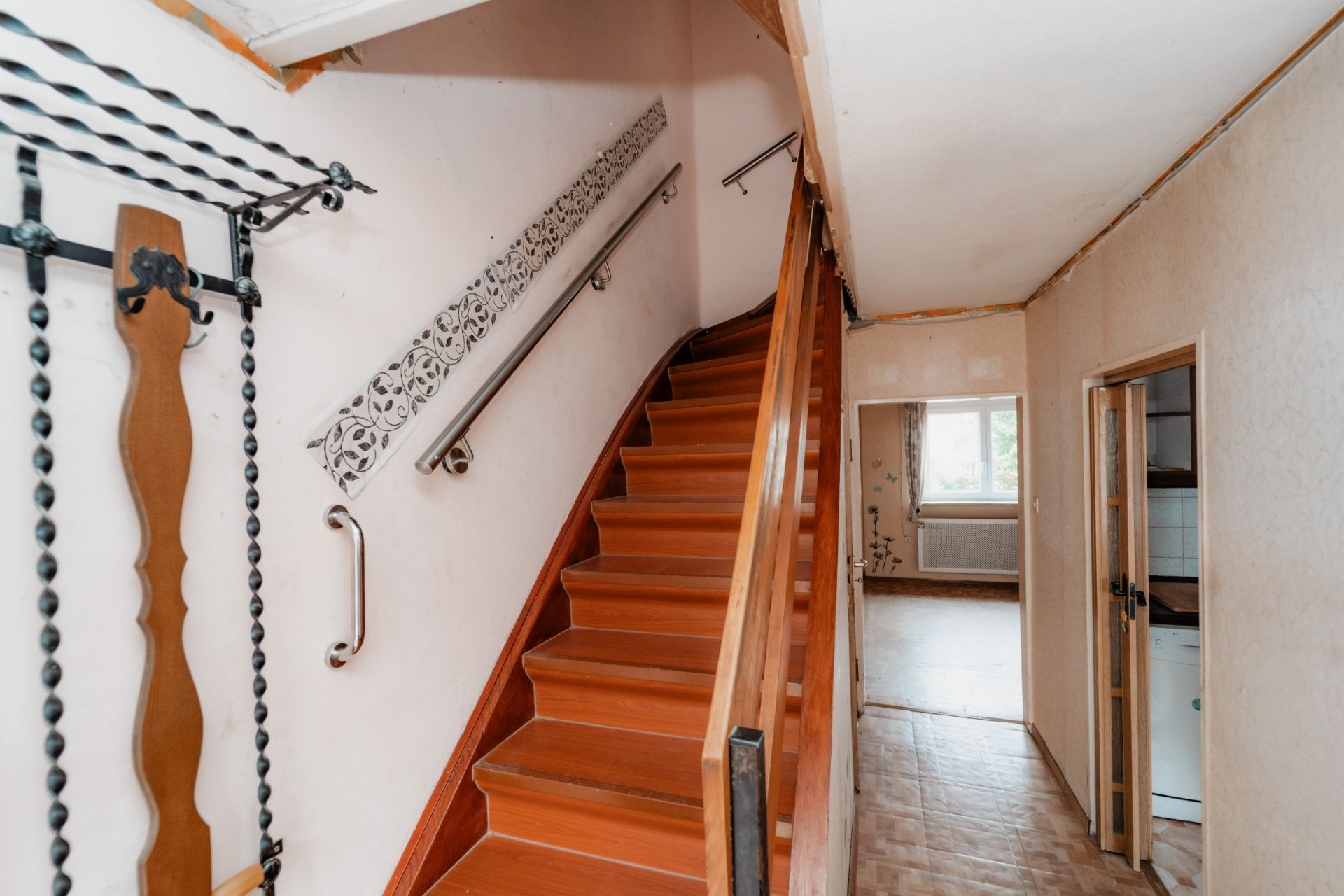 Flur mit Holztreppe, Wanddeko, Türen und Blick in ein helles Zimmer mit Fenster.
