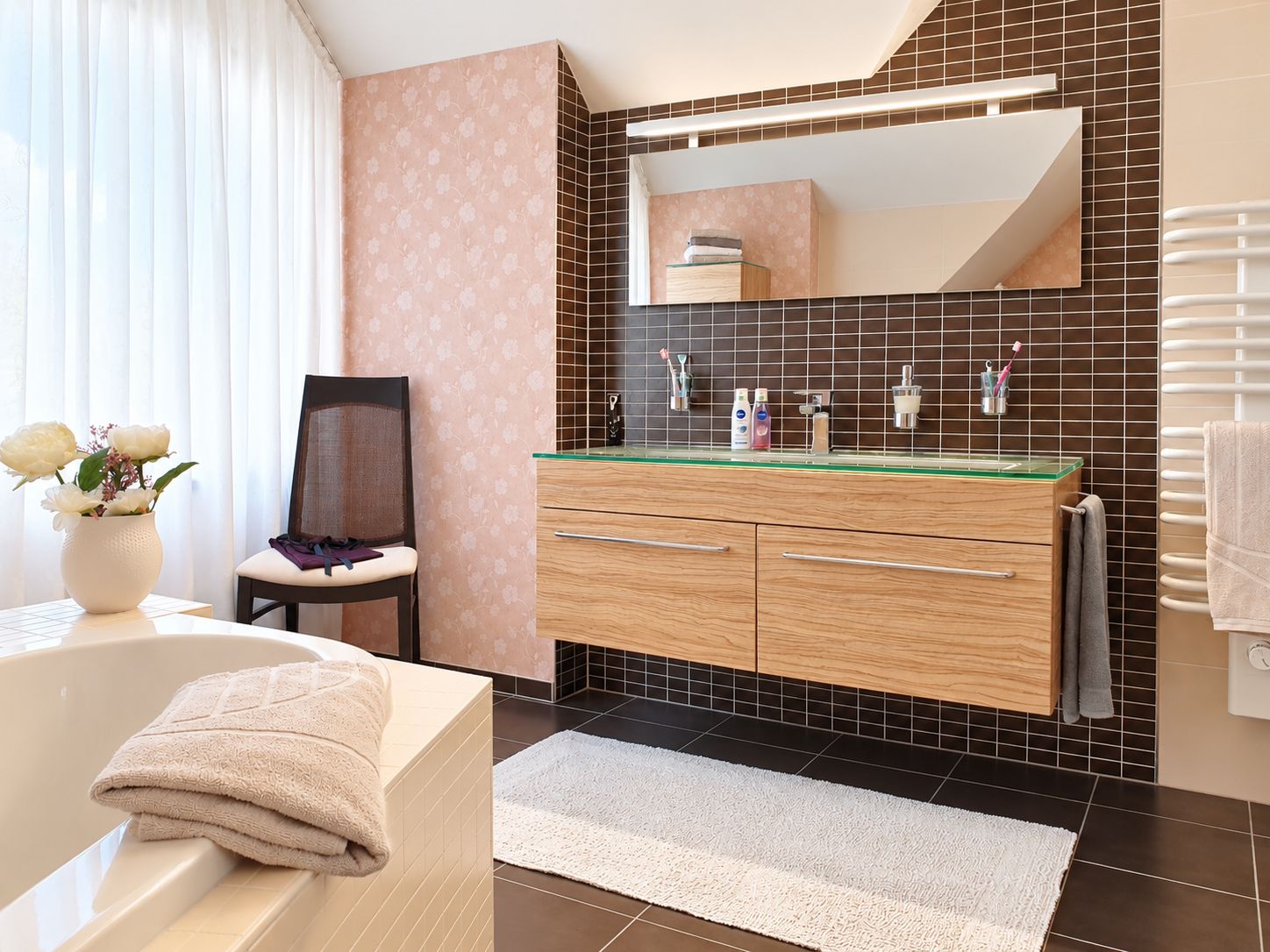 Modernes Bad mit Holz-Waschtisch, großem Spiegel, Badewanne und Stuhl am Fenster.