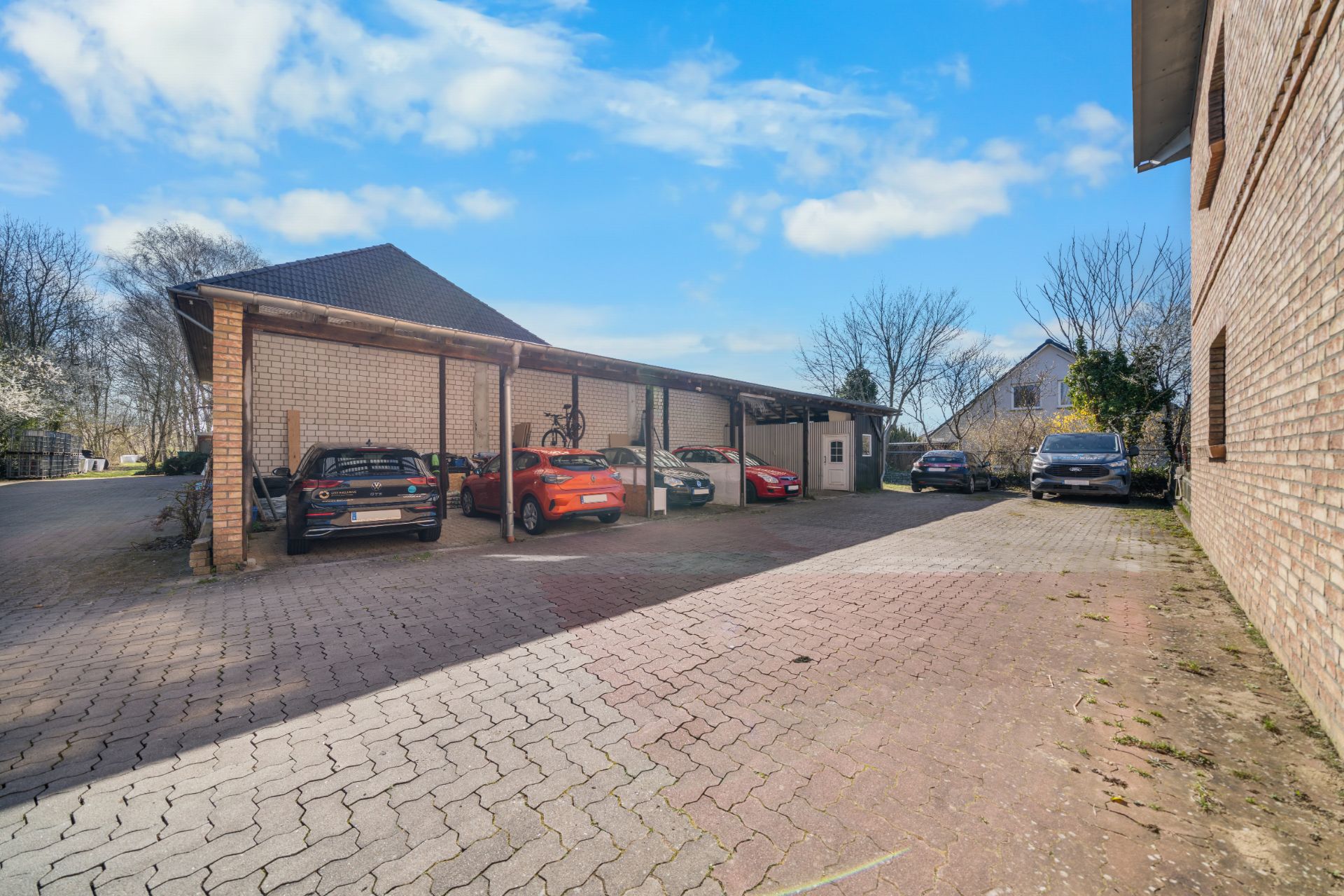 Überdachter Carport mit mehreren geparkten Autos und Fahrrädern neben einem Wohnhaus.