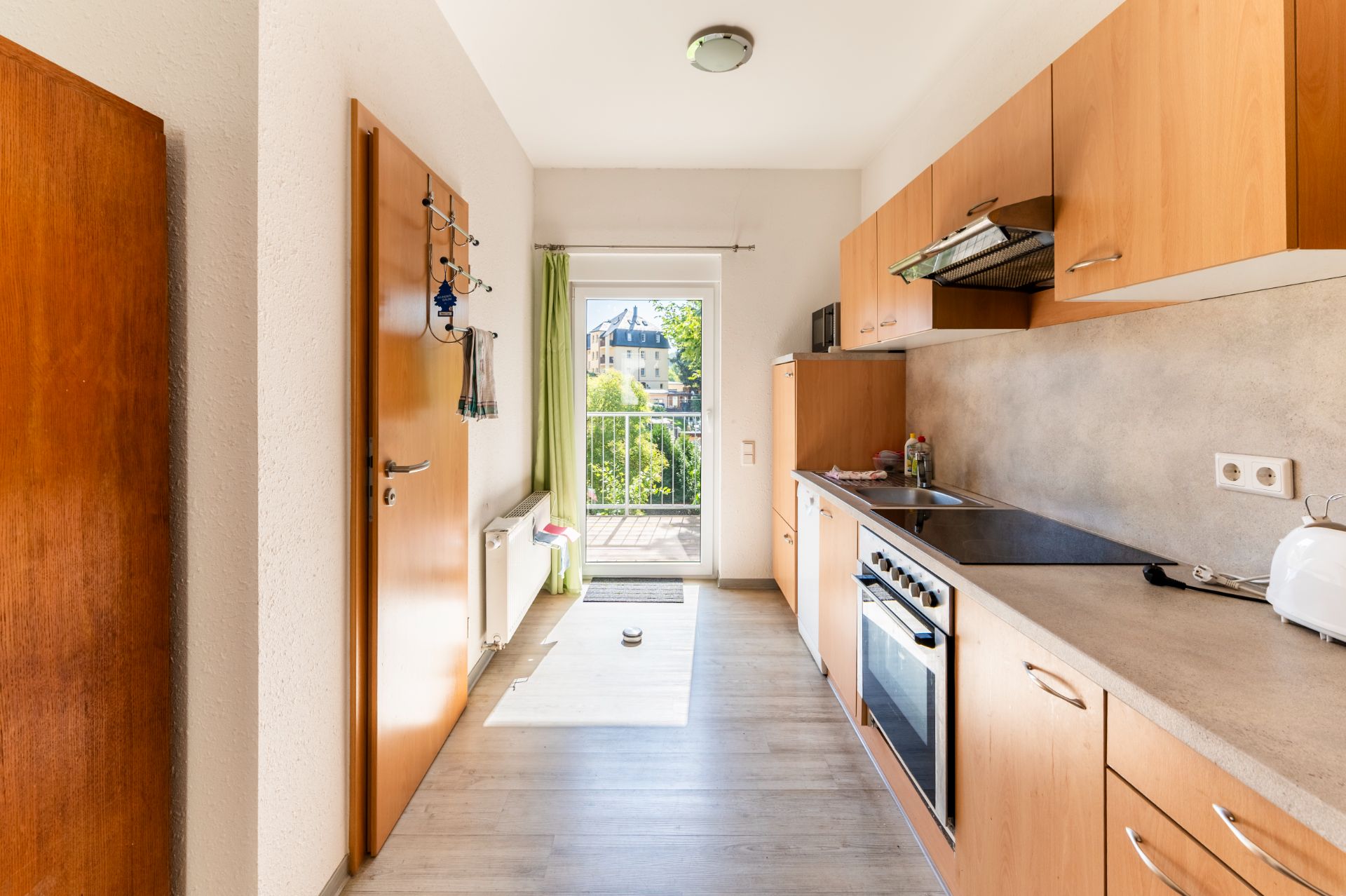 Helle Küche mit Holzmöbeln, Elektroherd und Zugang zu einem Balkon mit grünem Ausblick.