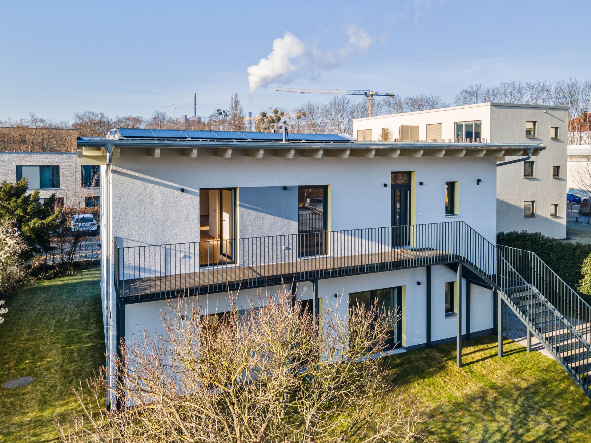 Modernes, zweistöckiges Wohnhaus mit Balkon und Außentreppe auf grünem Grundstück.