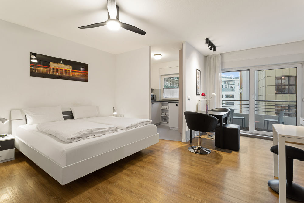 Modernes Schlafzimmer mit Doppelbett, Essbereich, kleiner Küche und Balkonzugang.