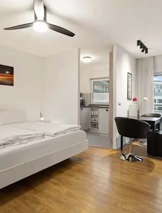 Modernes Schlafzimmer mit Doppelbett, Essbereich, kleiner Küche und Balkonzugang.