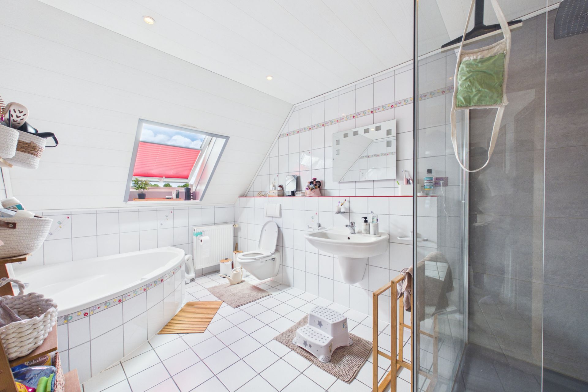 Helles Badezimmer mit Badewanne, Dusche, WC, Waschbecken und Fenster, weiß gefliest.