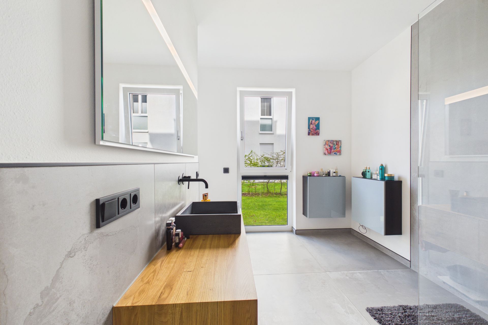 Modernes Badezimmer mit großem Spiegel, Waschbecken, Holzmöbel und Glasdusche, Tür zum Garten.