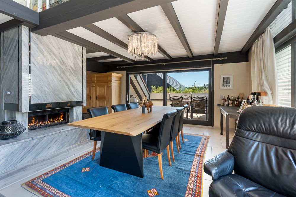 Esszimmer mit Holztisch, schwarzen Stühlen, Kamin, großem Fenster und blauem Teppich.