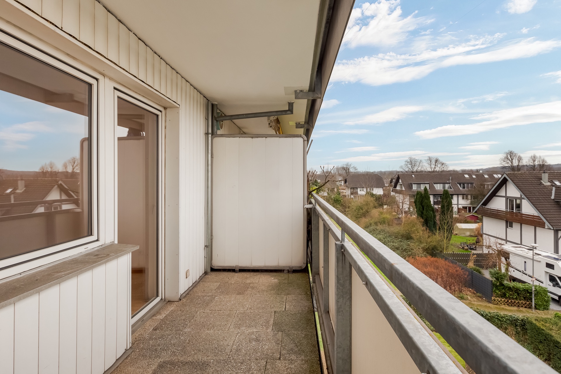 Balkon mit Blick auf Wohnhäuser und Garten, angrenzend an weiße Hausfassade.