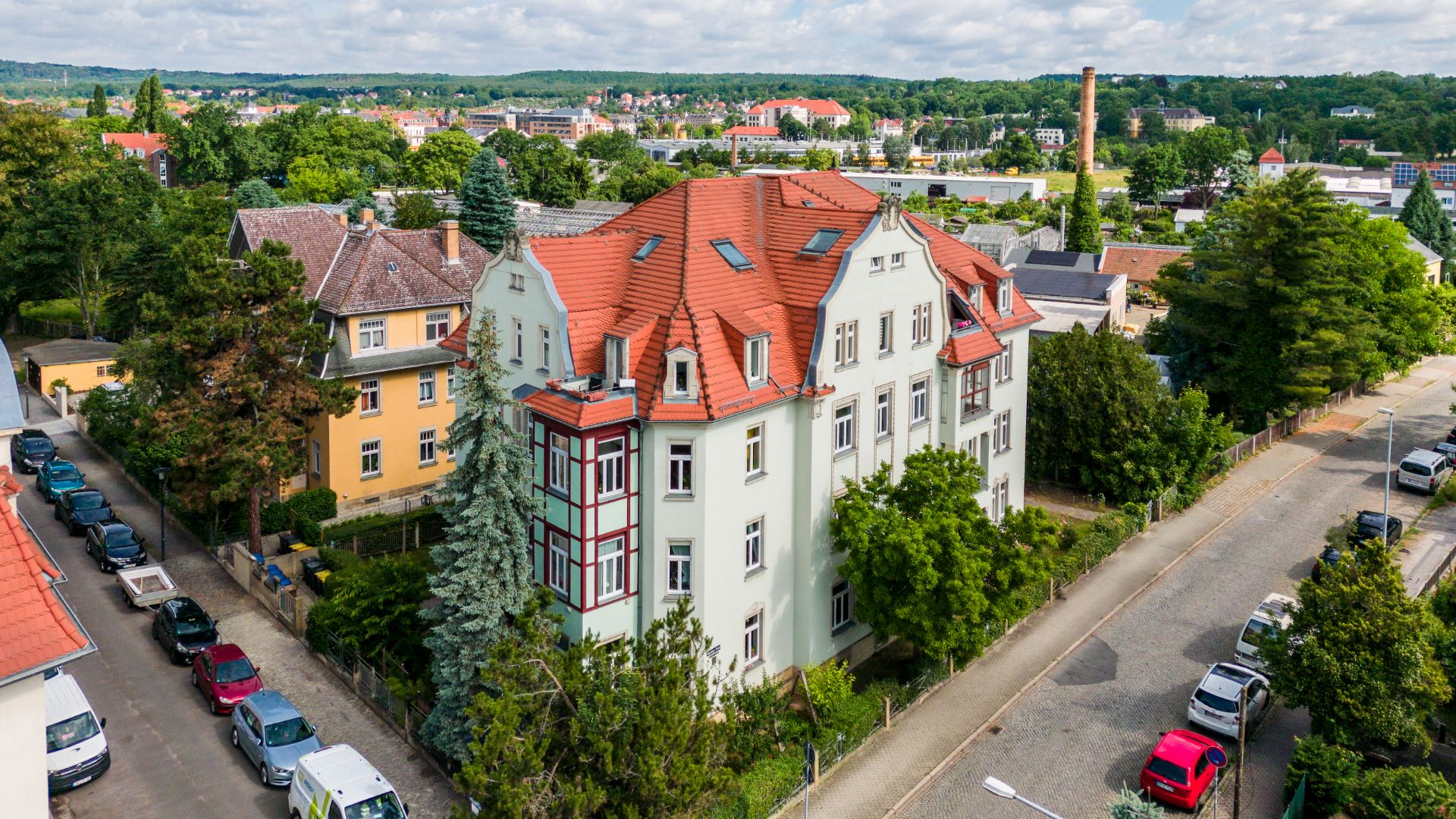 Mehrstöckiges Wohnhaus mit rotem Dach und Bäumen in einer ruhigen Wohngegend.