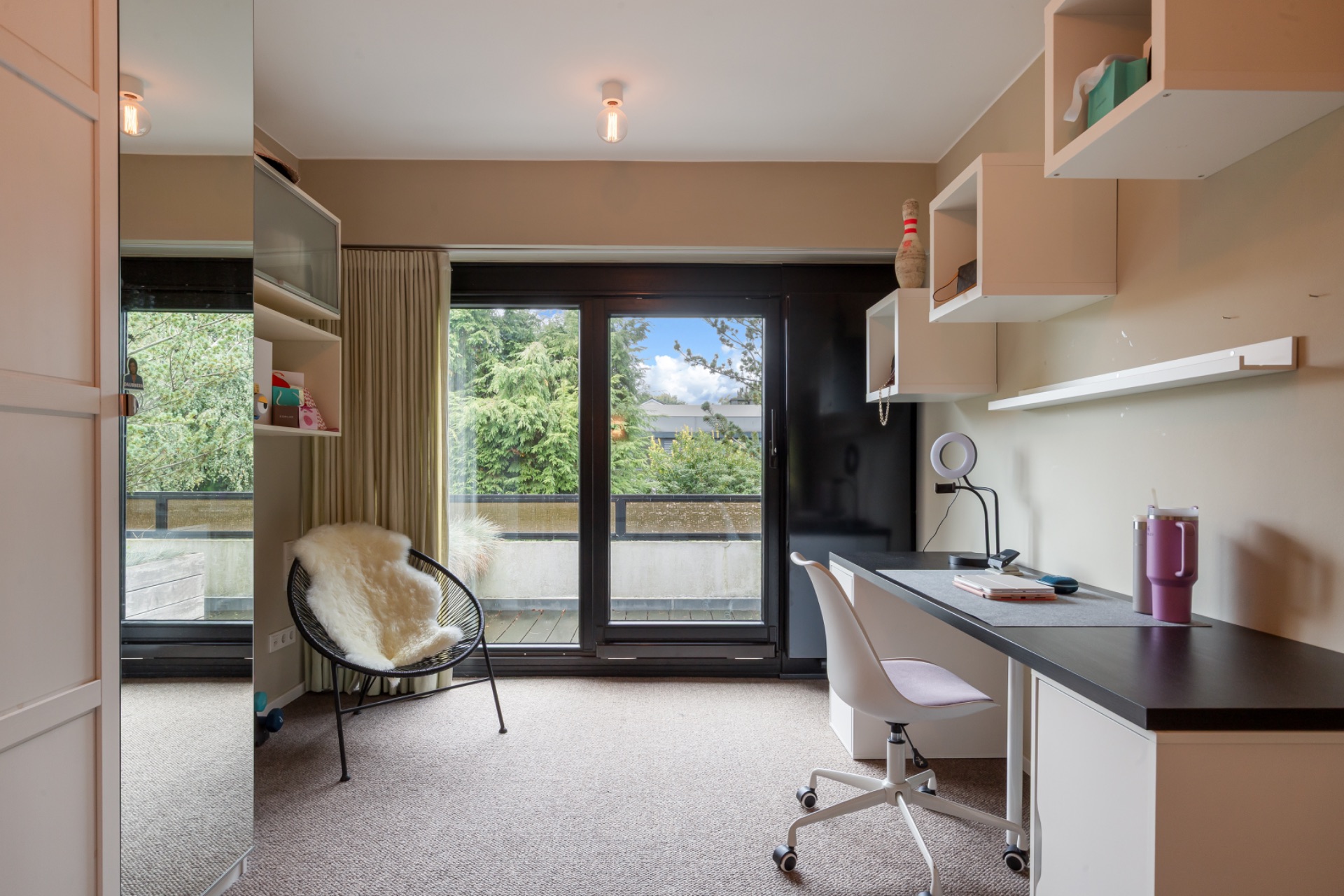 Helles Arbeitszimmer mit Schreibtisch, Stuhl, Regal und großem Fenster zur Terrasse.