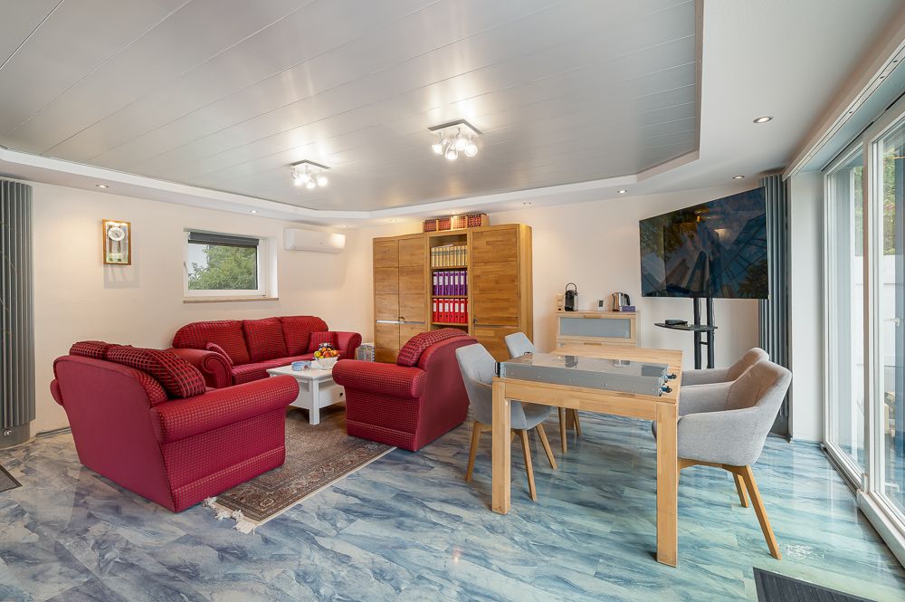 Wohnzimmer mit roten Sofas, Holztisch, Regalen und großem Fenster.