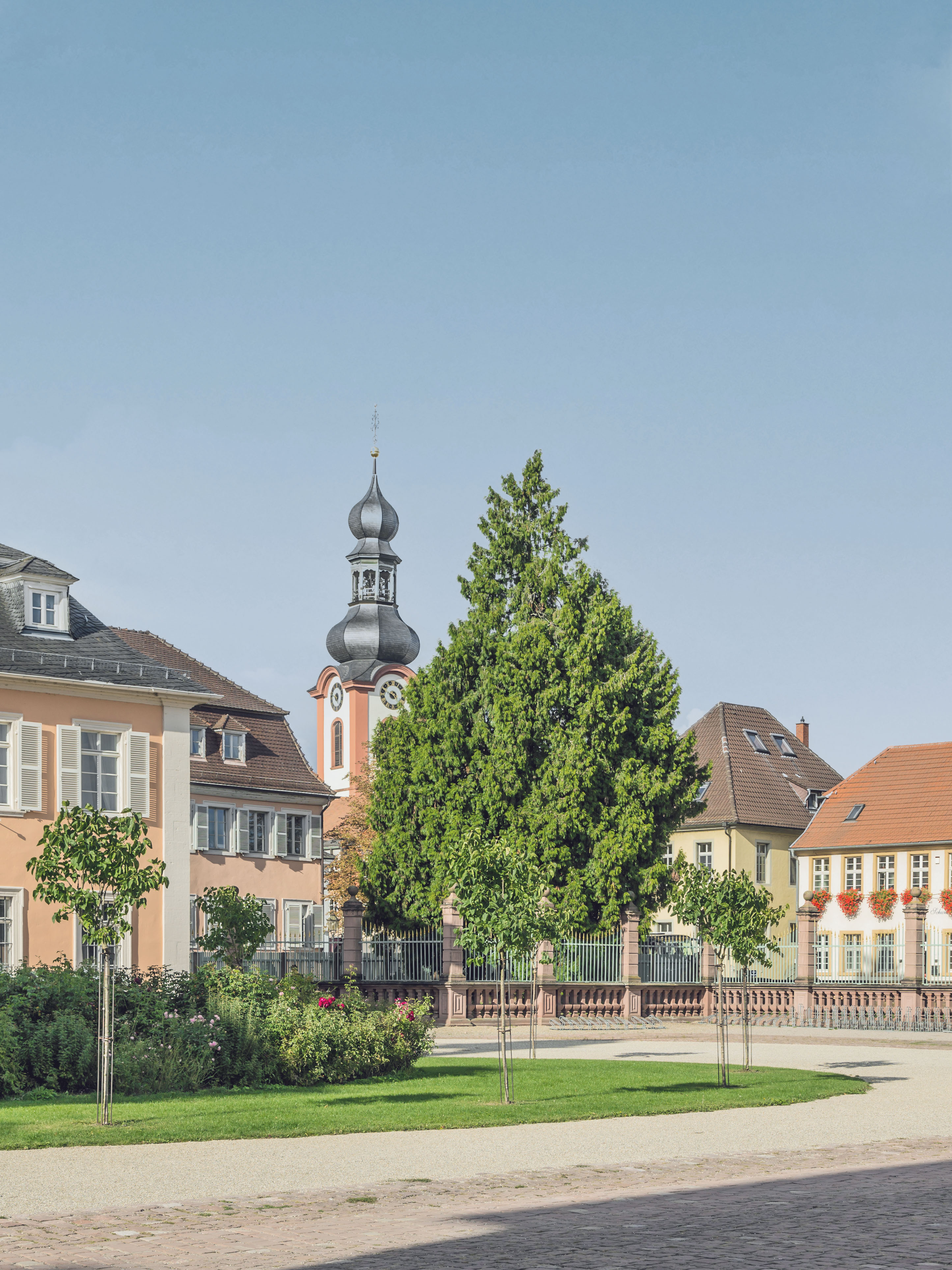 Mehrere Wohnhäuser und ein Kirchturm hinter einem begrünten, gepflegten Vorgarten.