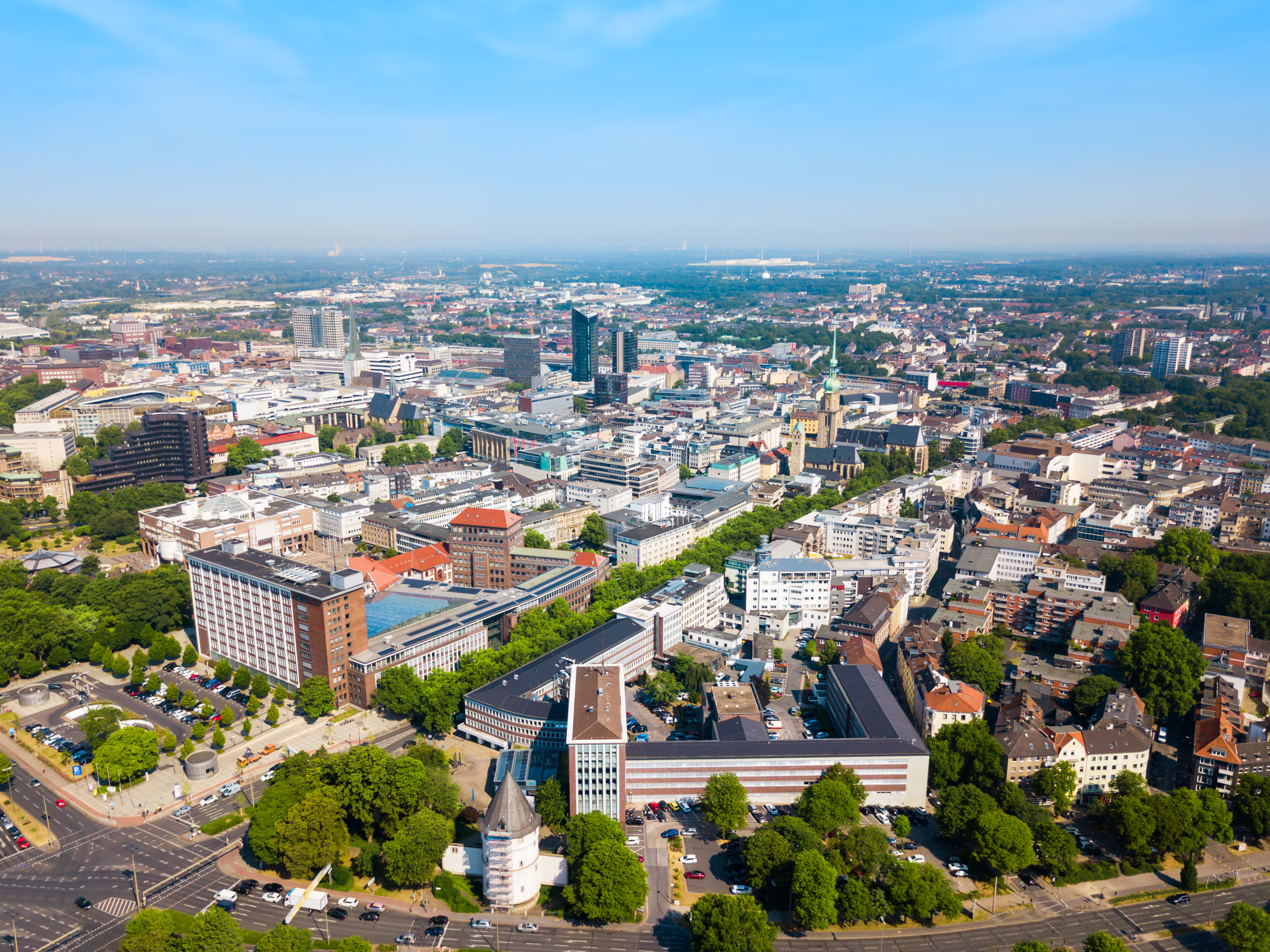 Luftaufnahme einer Stadt mit vielen Gebäuden und grünen Bäumen unter blauem Himmel.
