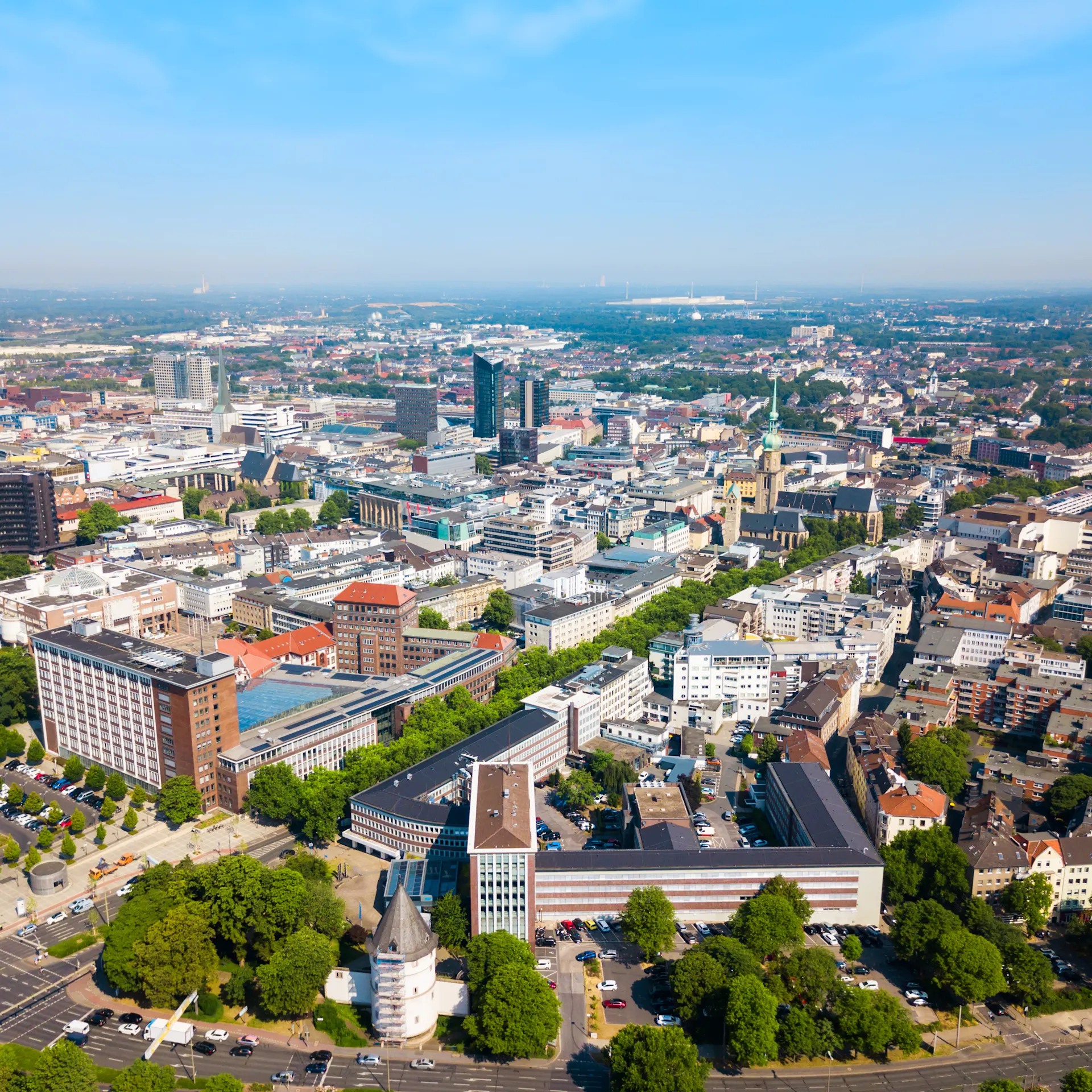 Luftaufnahme einer Stadt mit vielen Gebäuden und grünen Bäumen unter blauem Himmel.