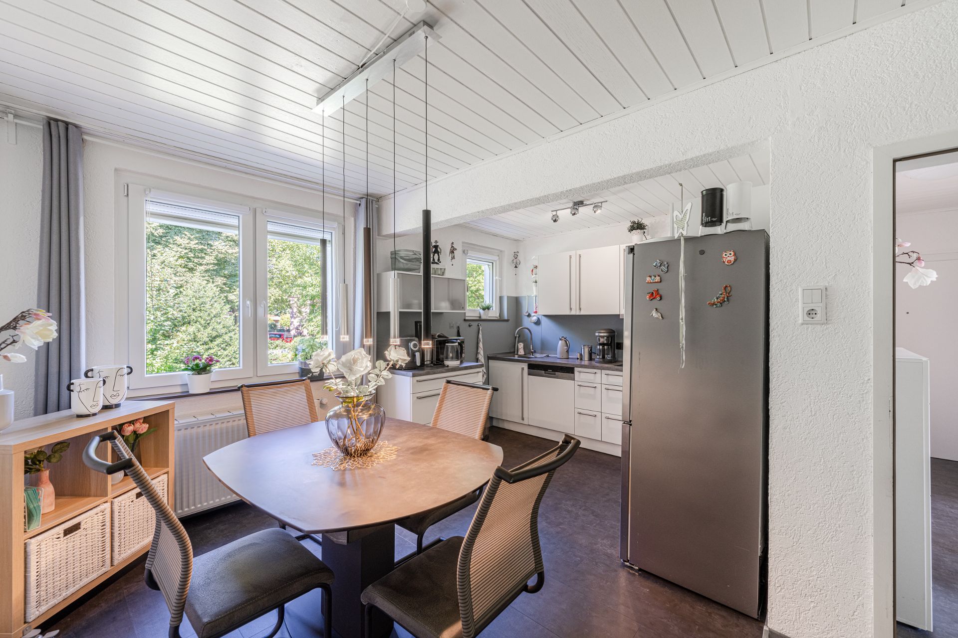 Moderne Wohnküche mit Esstisch, Kühlschrank und Fenstern mit Blick ins Grüne.