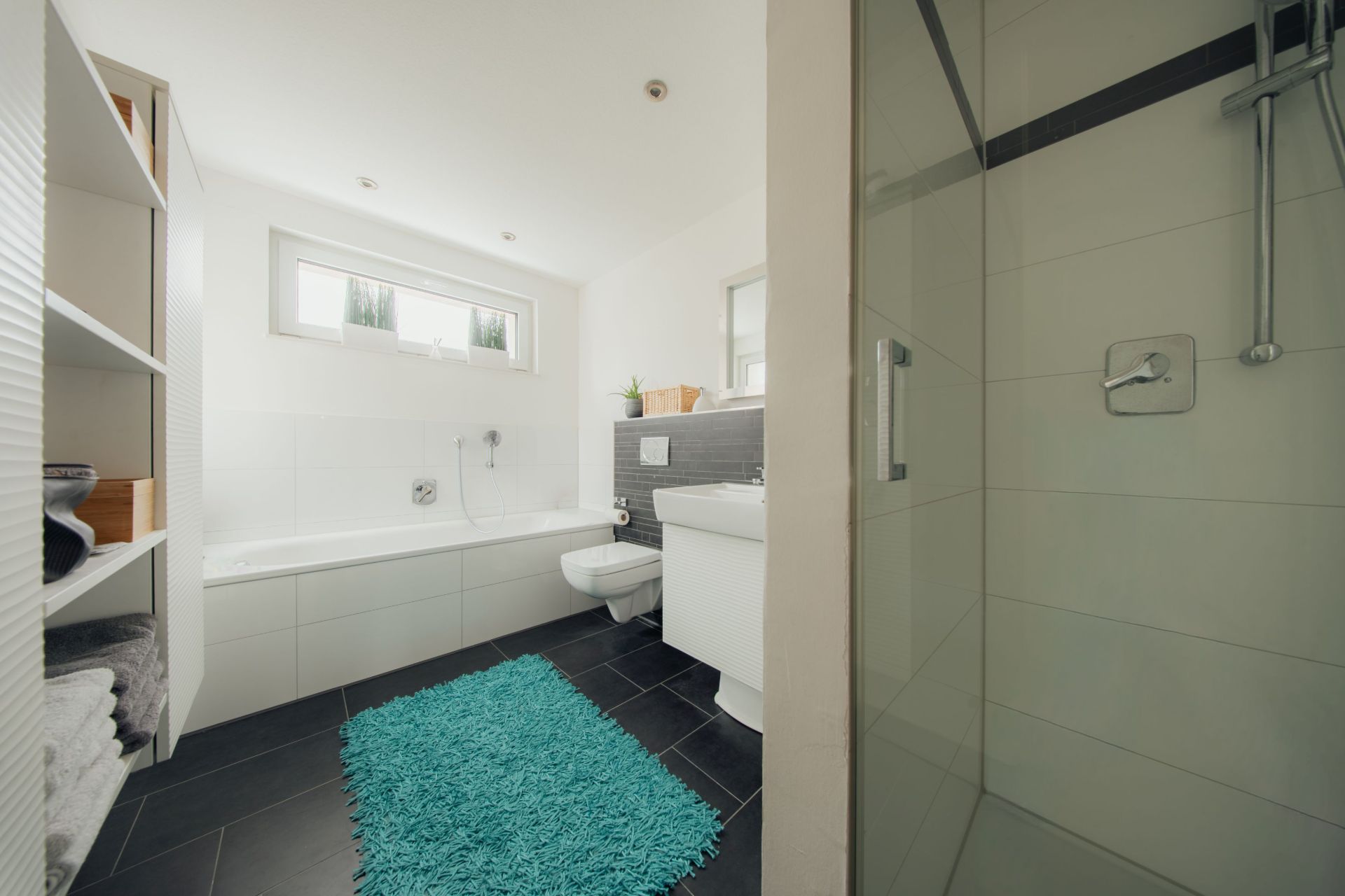 Modernes Badezimmer mit Dusche, Badewanne, Toilette, Waschbecken und blauem Teppich.