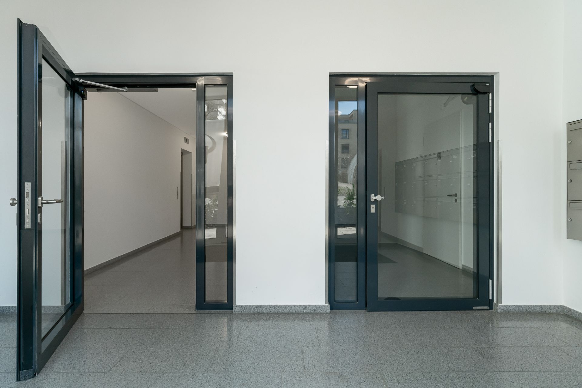 Heller Eingangsbereich mit zwei Glastüren und Briefkästen an der Wand.
