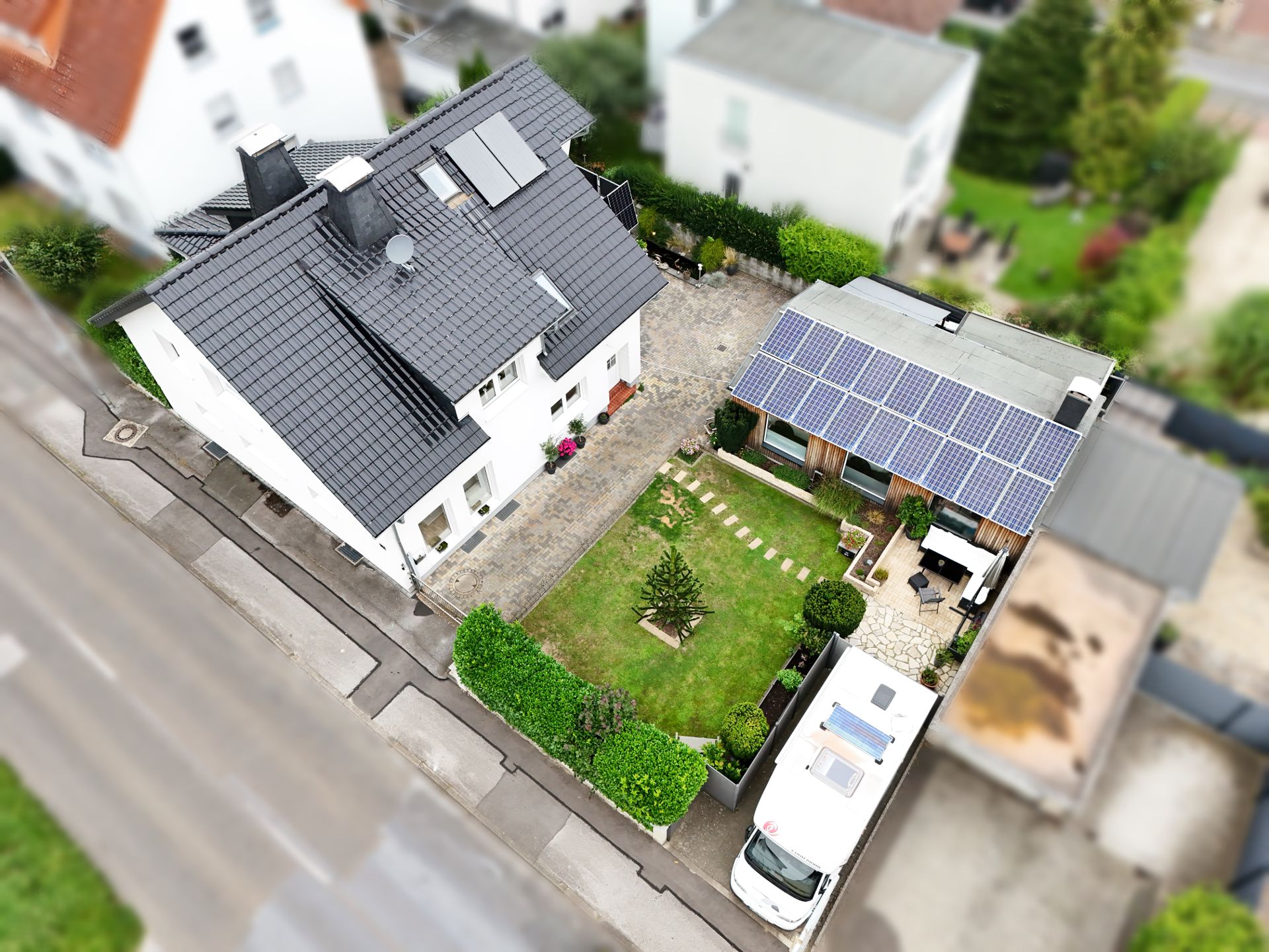 Luftaufnahme eines Wohnhauses mit Garten, Garage mit Solarpanelen und geparktem Wohnmobil.