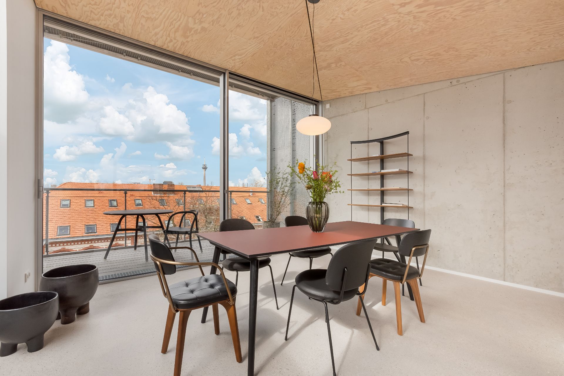 Esszimmer mit großem Tisch, sechs Stühlen, Regal, Blumen und Zugang zum Balkon mit Stadtblick.