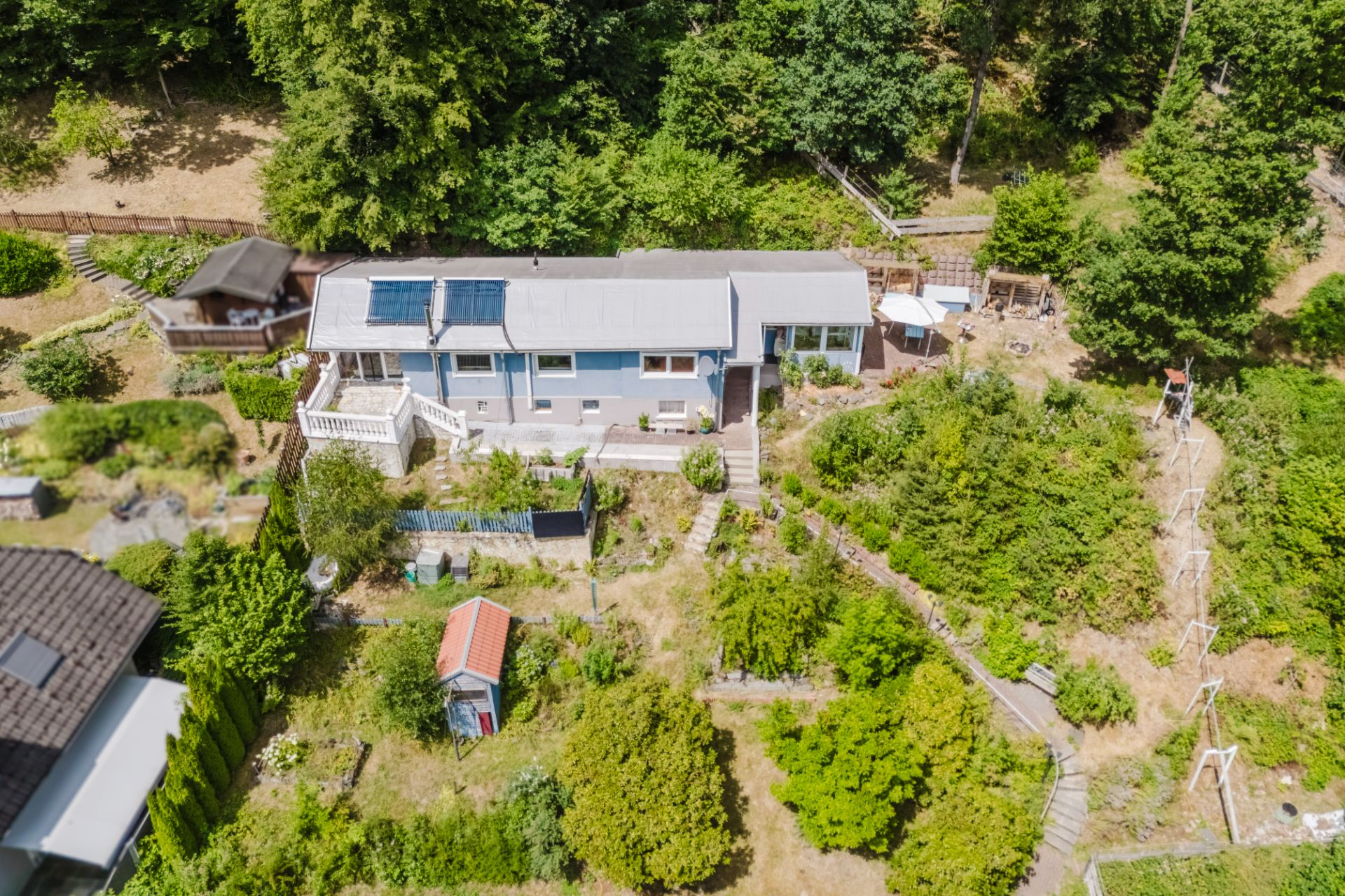 Luftaufnahme eines Einfamilienhauses mit Garten und umliegenden Bäumen.