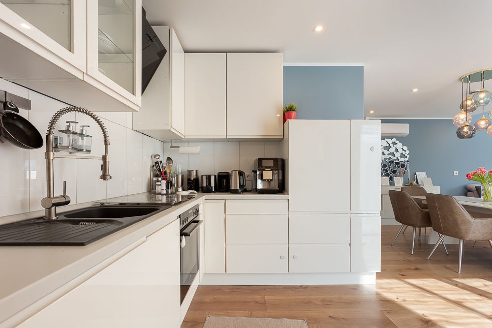 Moderne weiße Einbauküche mit Geräten, neben einem Essbereich mit Tisch und Stühlen.