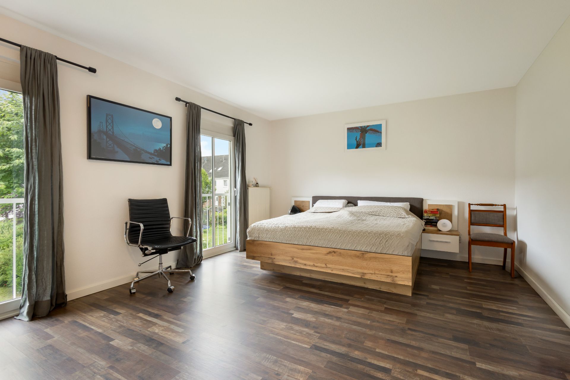 Helles Schlafzimmer mit Doppelbett, Stuhl, großem Fenster und Holzfußboden.