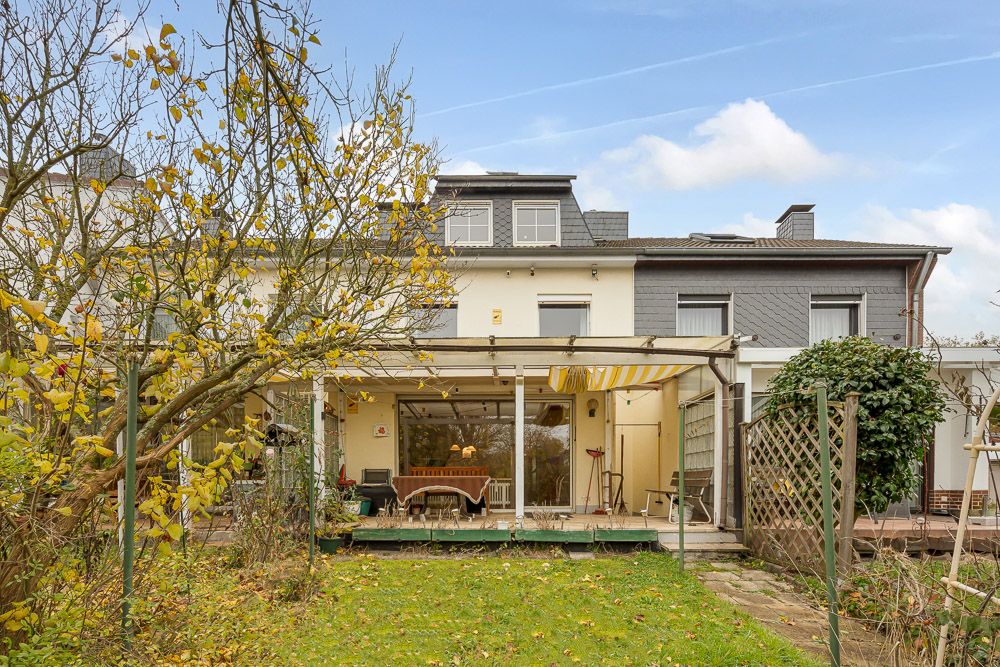 Rückseite eines Hauses mit Terrasse, Gartentisch, Stühlen und Herbstbäumen im Garten.