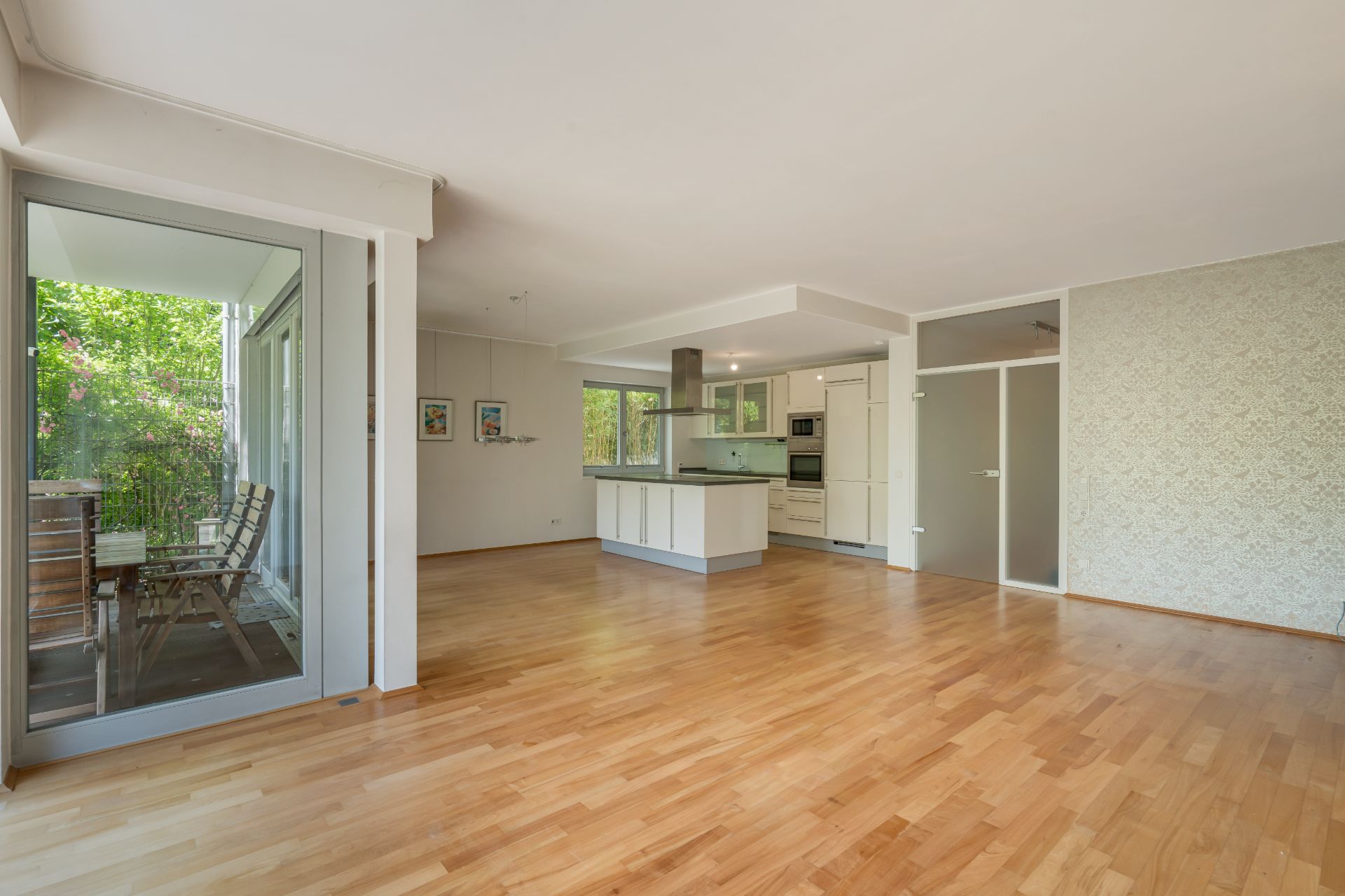 Helles Wohnzimmer mit Parkettboden, offener Küche und Zugang zu verglastem Balkon.