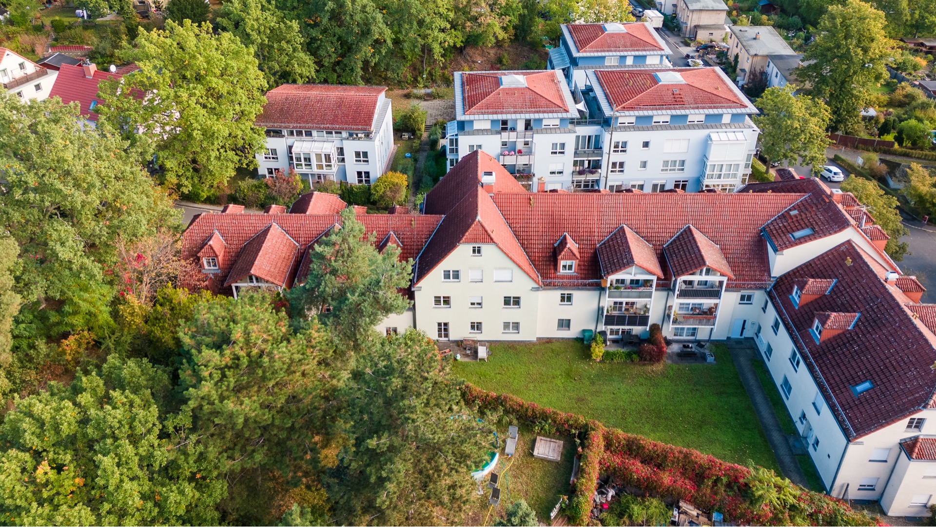 Luftaufnahme von Wohnhäusern mit roten Dächern und begrüntem Garten.