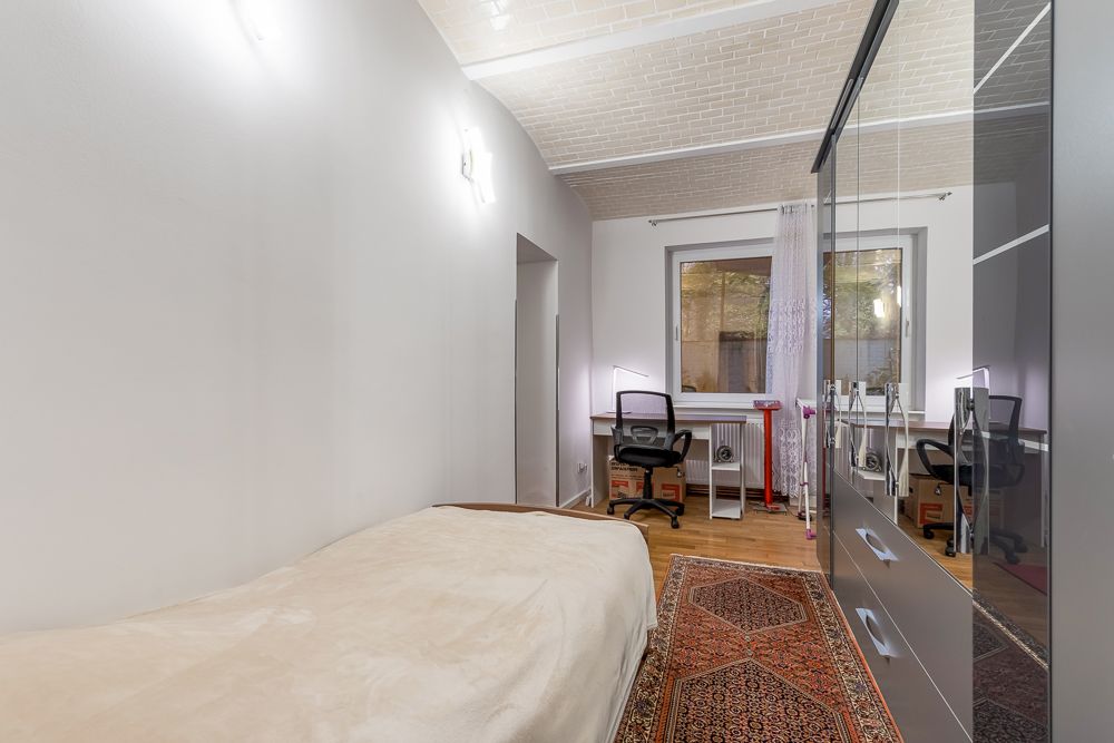 Schlafzimmer mit Einzelbett, Schreibtisch am Fenster, Kleiderschrank und Teppich.