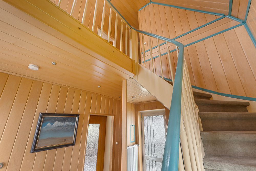 Treppe mit beige-blauen Geländern in einem holzverkleideten Flur, Gemälde an der Wand.