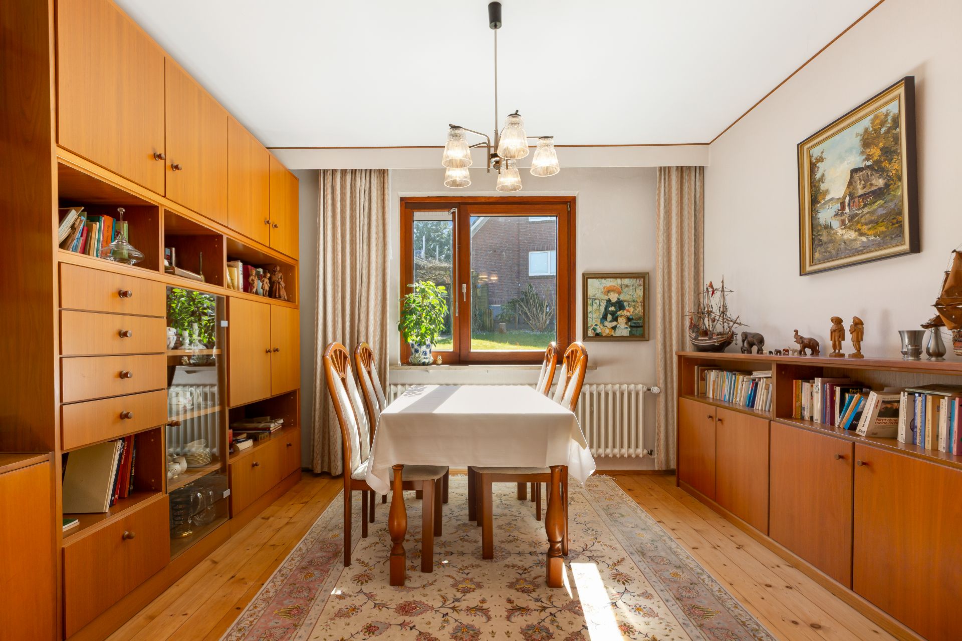 Esszimmer mit Holzmöbeln, Bücherregalen, Tisch, sechs Stühlen und großem Fenster.