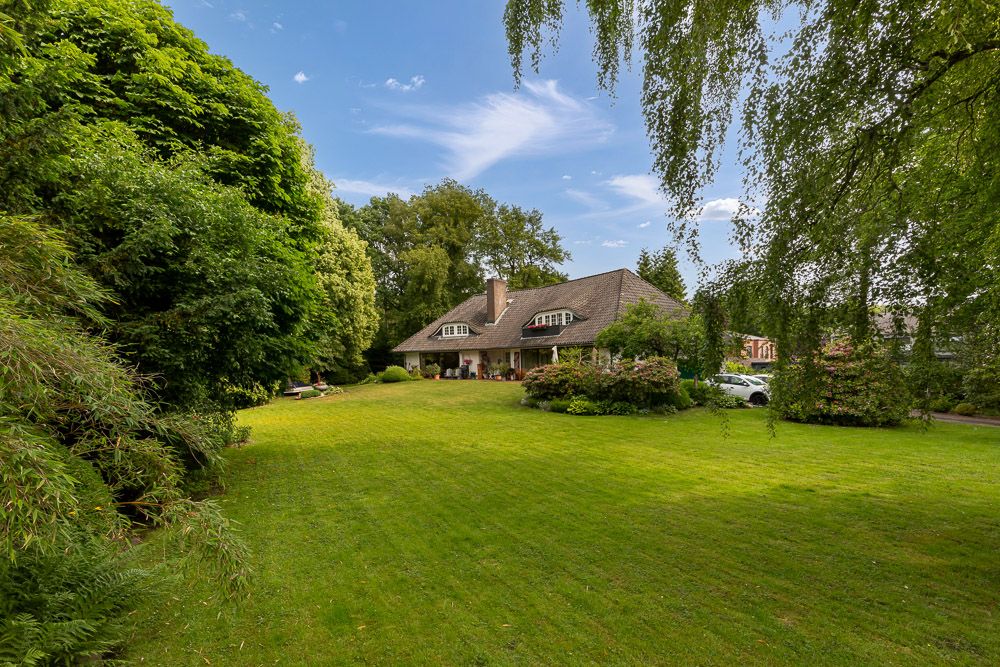 Großes Einfamilienhaus mit Garten, umgeben von Rasen und Bäumen, unter blauem Himmel.