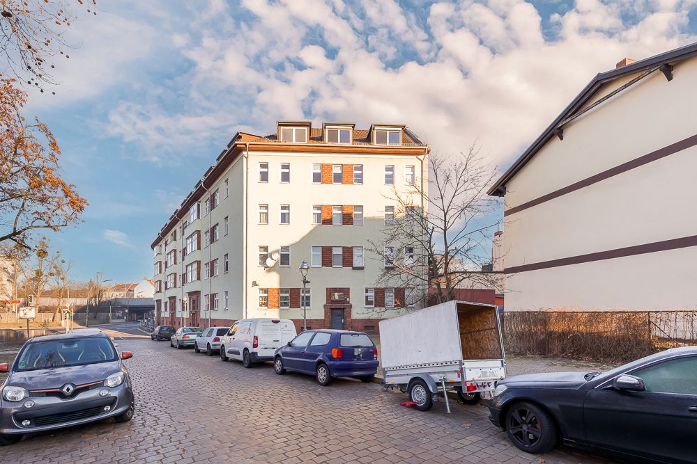 Mehrstöckiges Wohnhaus mit geparkten Autos und Anhänger an einer gepflasterten Straße.