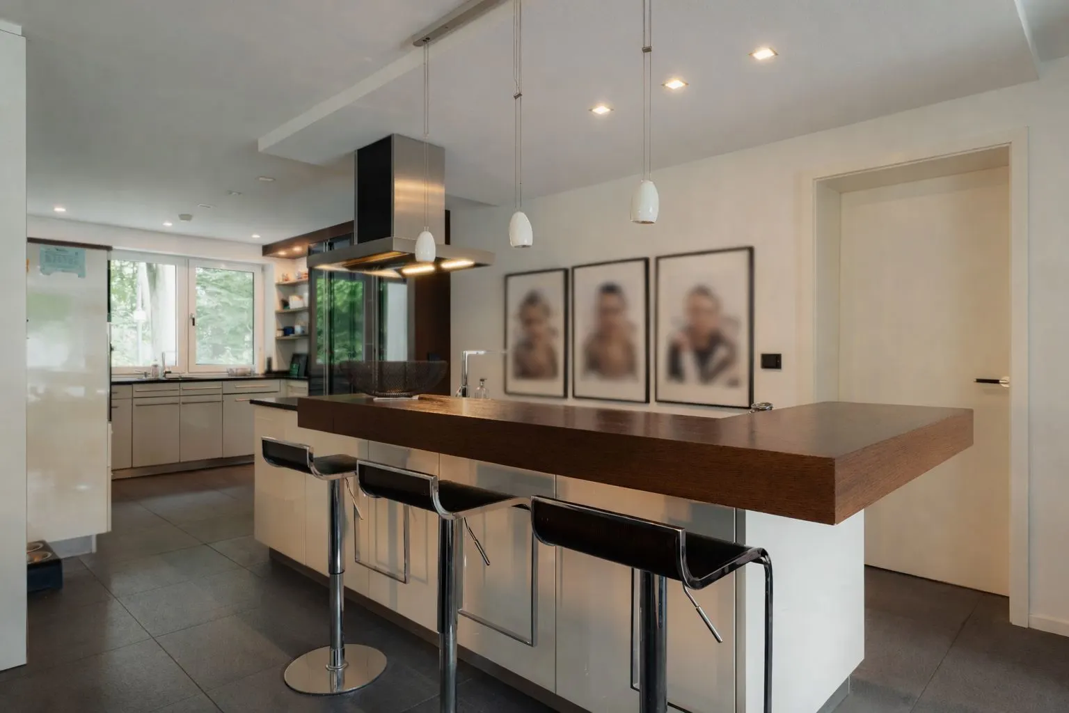 Moderne Küche mit Kücheninsel, drei Barhockern und drei gerahmten Bildern an der Wand.