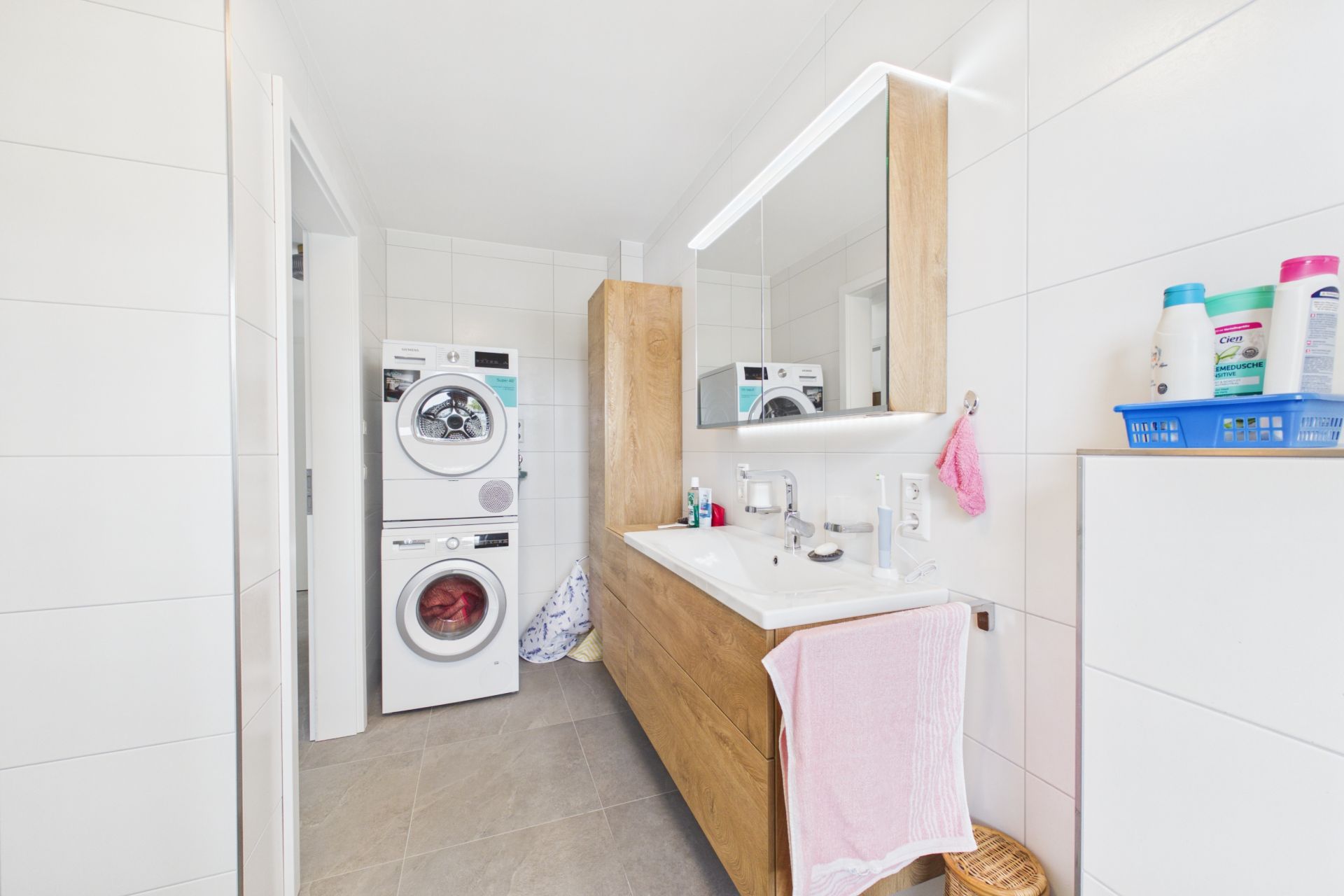 Helles Badezimmer mit Waschmaschine, Trockner, Doppelwaschbecken und Spiegelschrank.