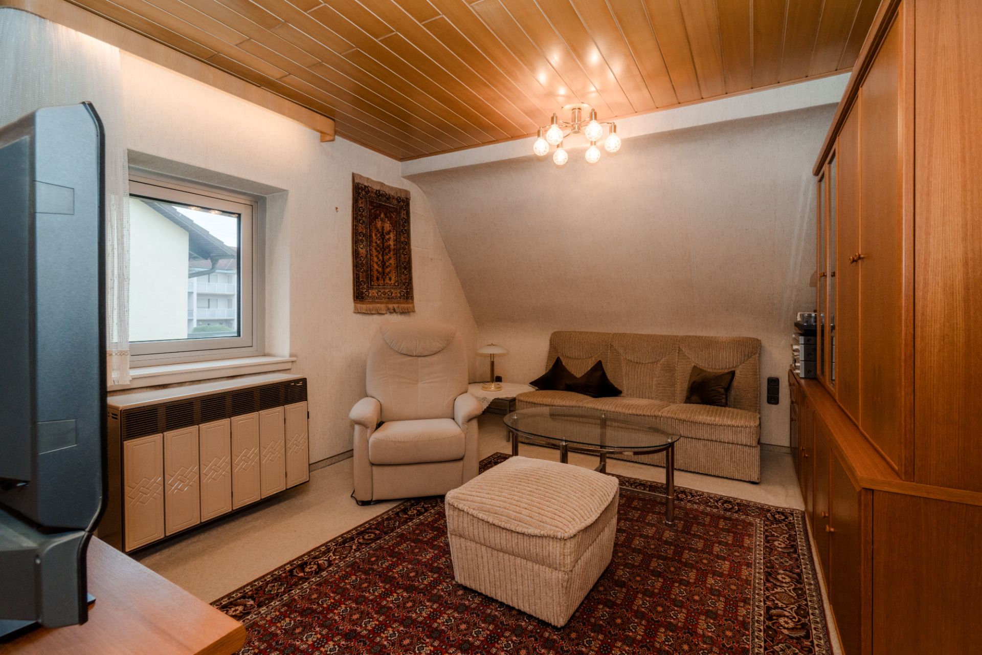 Wohnzimmer mit Sessel, Sofa, Teppich, Couchtisch, TV und Holzdecke.