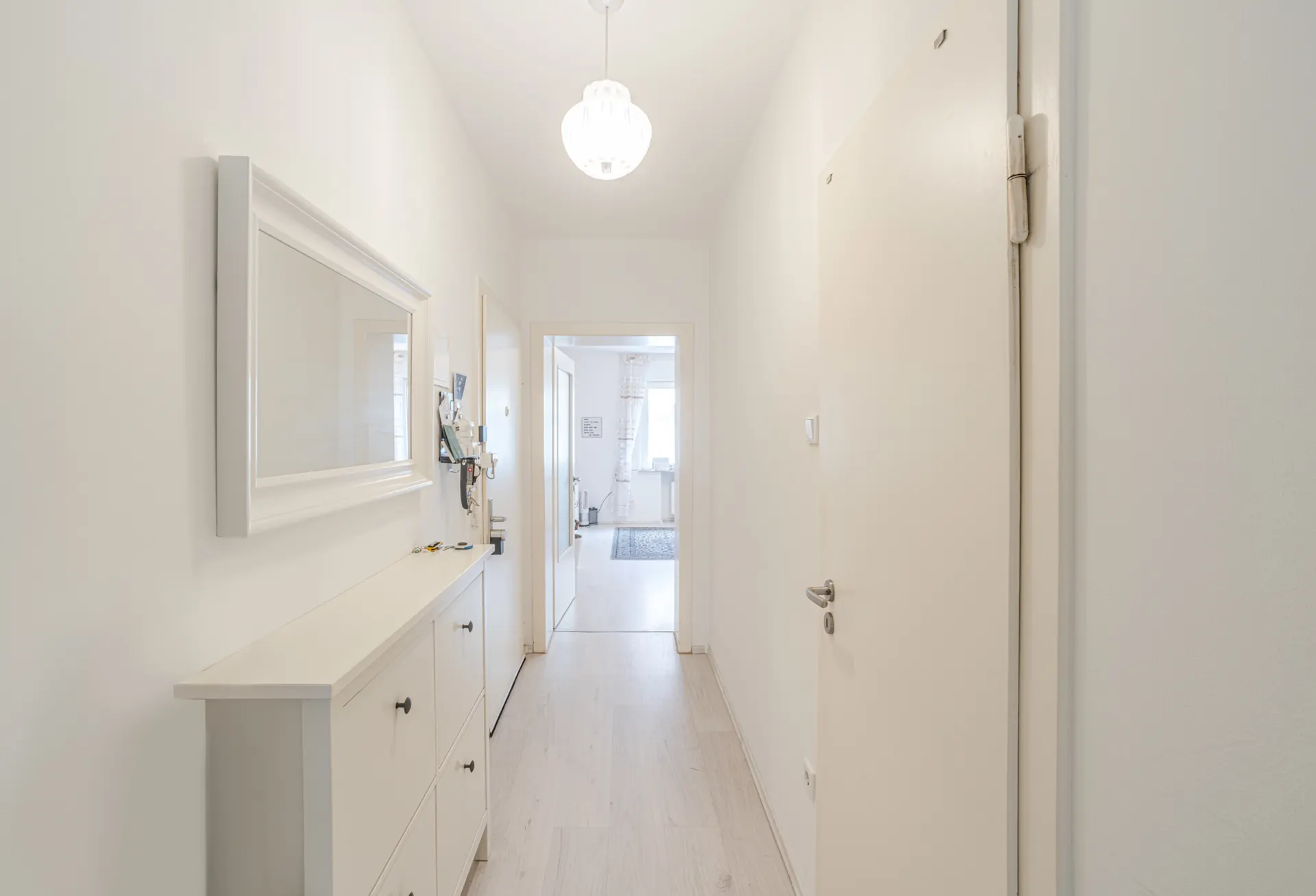 Heller Flur mit weißem Möbelstück, Spiegel und Lampe, Türen führen in weitere Räume.