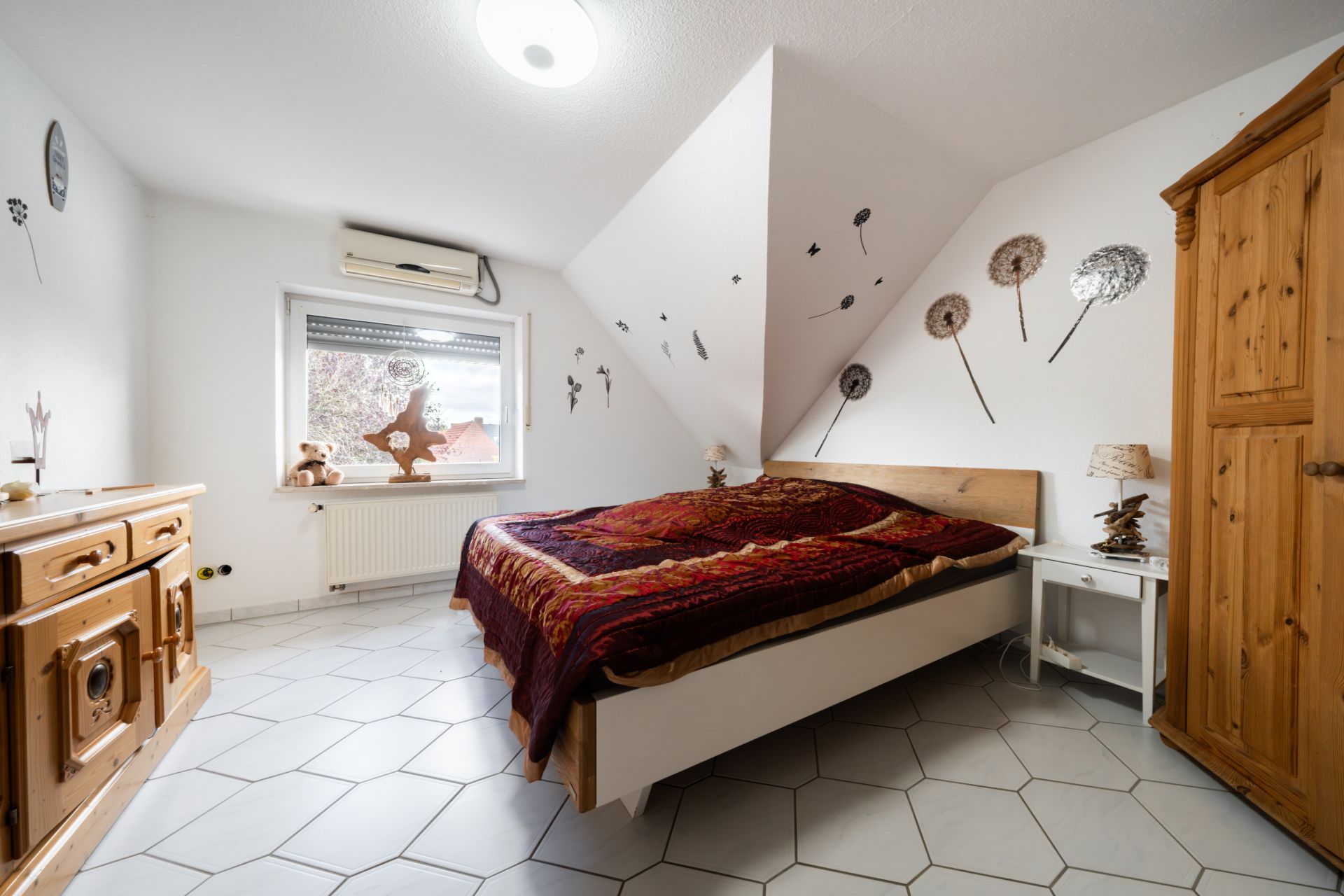 Helles Schlafzimmer mit Doppelbett, Holzschrank, Holzmöbeln und Wanddekorationen mit Pusteblumenmotiv.
